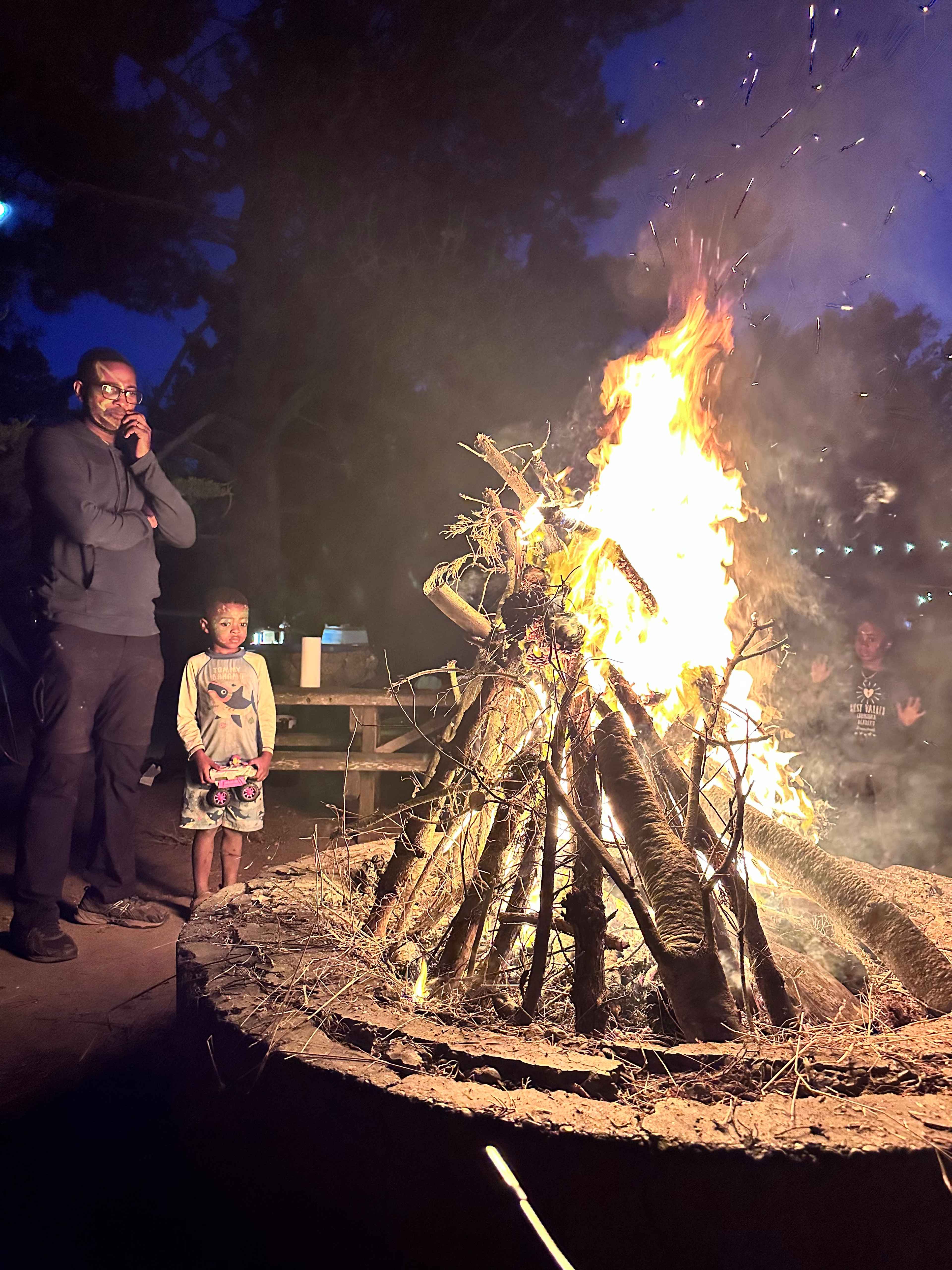 John and his young son standing beside a roaring teepee campfire that John built at Williams Grove group campground in Humboldt Redwoods State Park at dusk