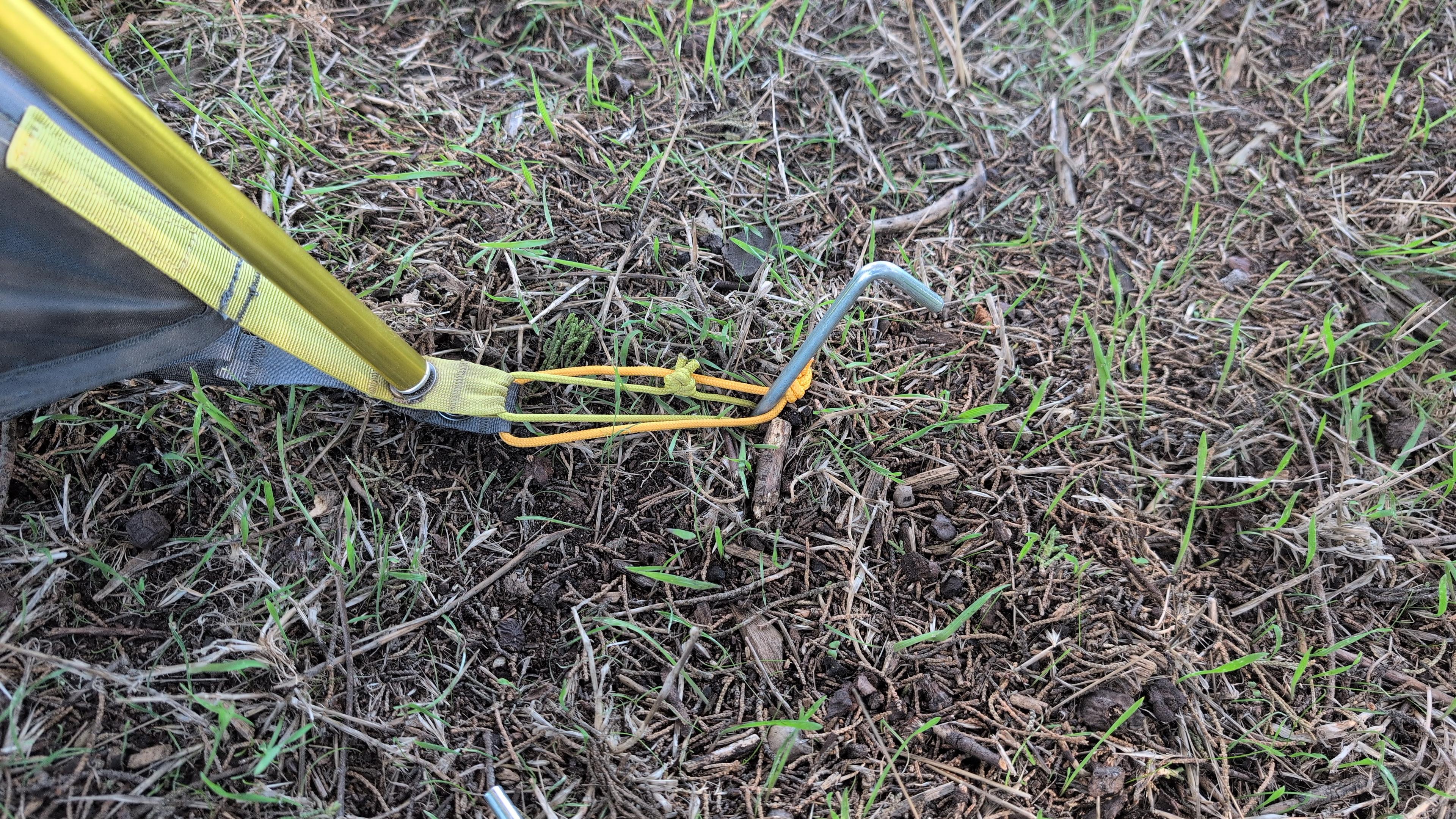 A tent stake being driven into the ground at the corner of a tent