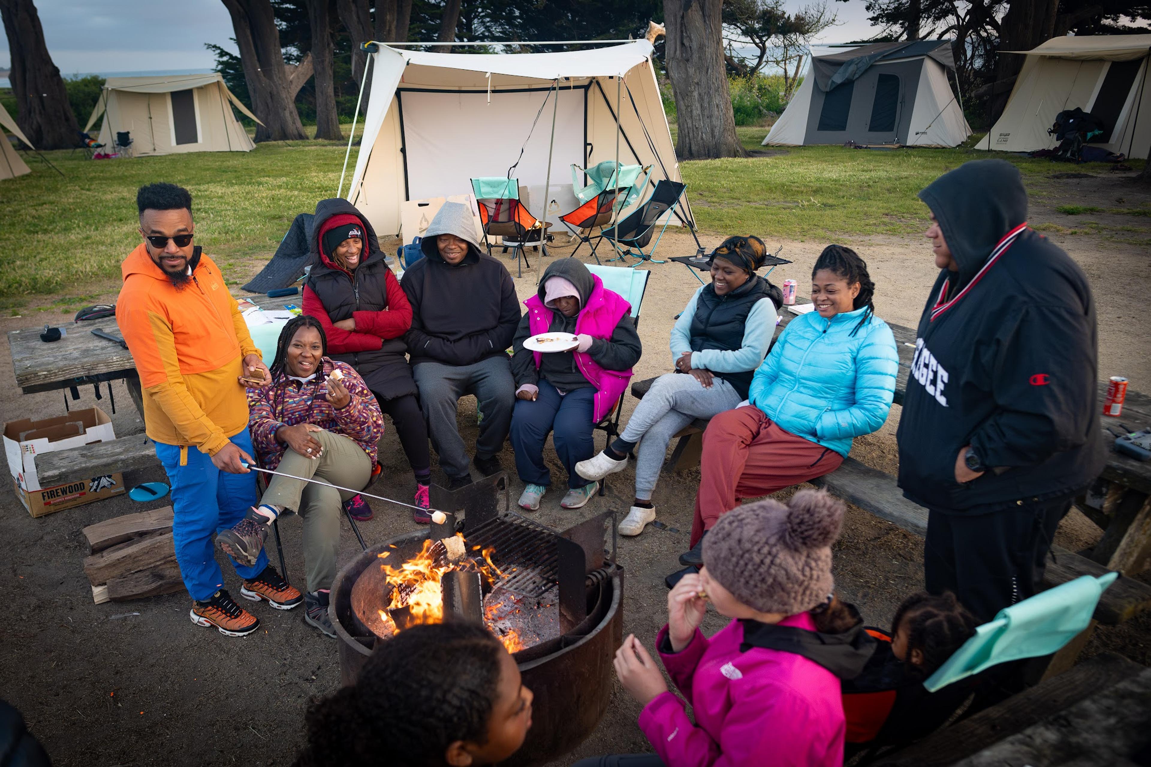 Outdoorithm Collective group of more than 15 people gathered around a campfire at Half Moon Bay State Beach during a community camping trip, kids and adults representing many backgrounds Outdoorithm Collective group of more than 15 people gathered around a campfire at Half Moon Bay State Beach during a community camping trip, kids and adults representing many backgrounds