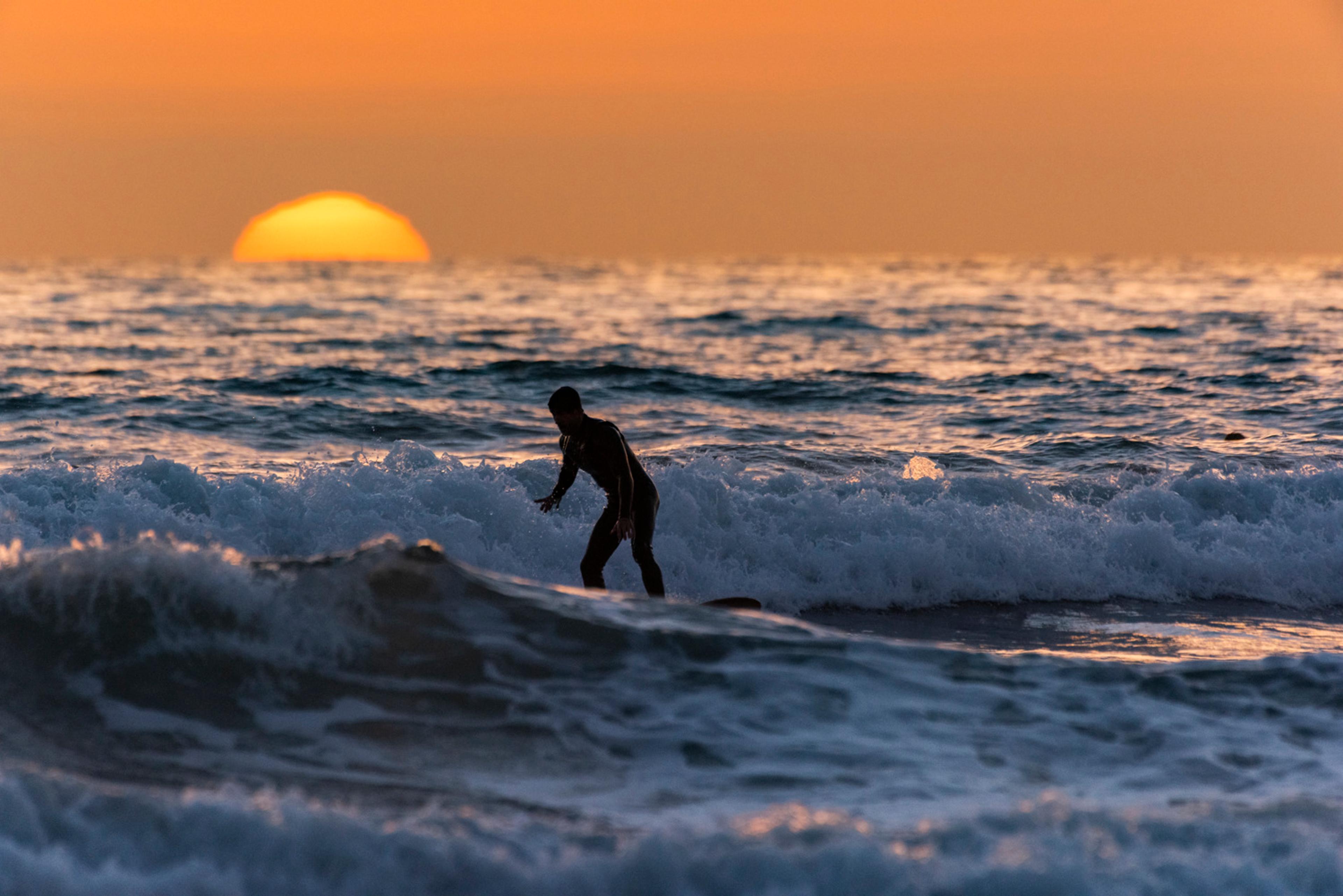 Surfer silhouetted against an orange sunset at San Elijo State Beach in Encinitas Surfer silhouetted against an orange sunset at San Elijo State Beach in Encinitas