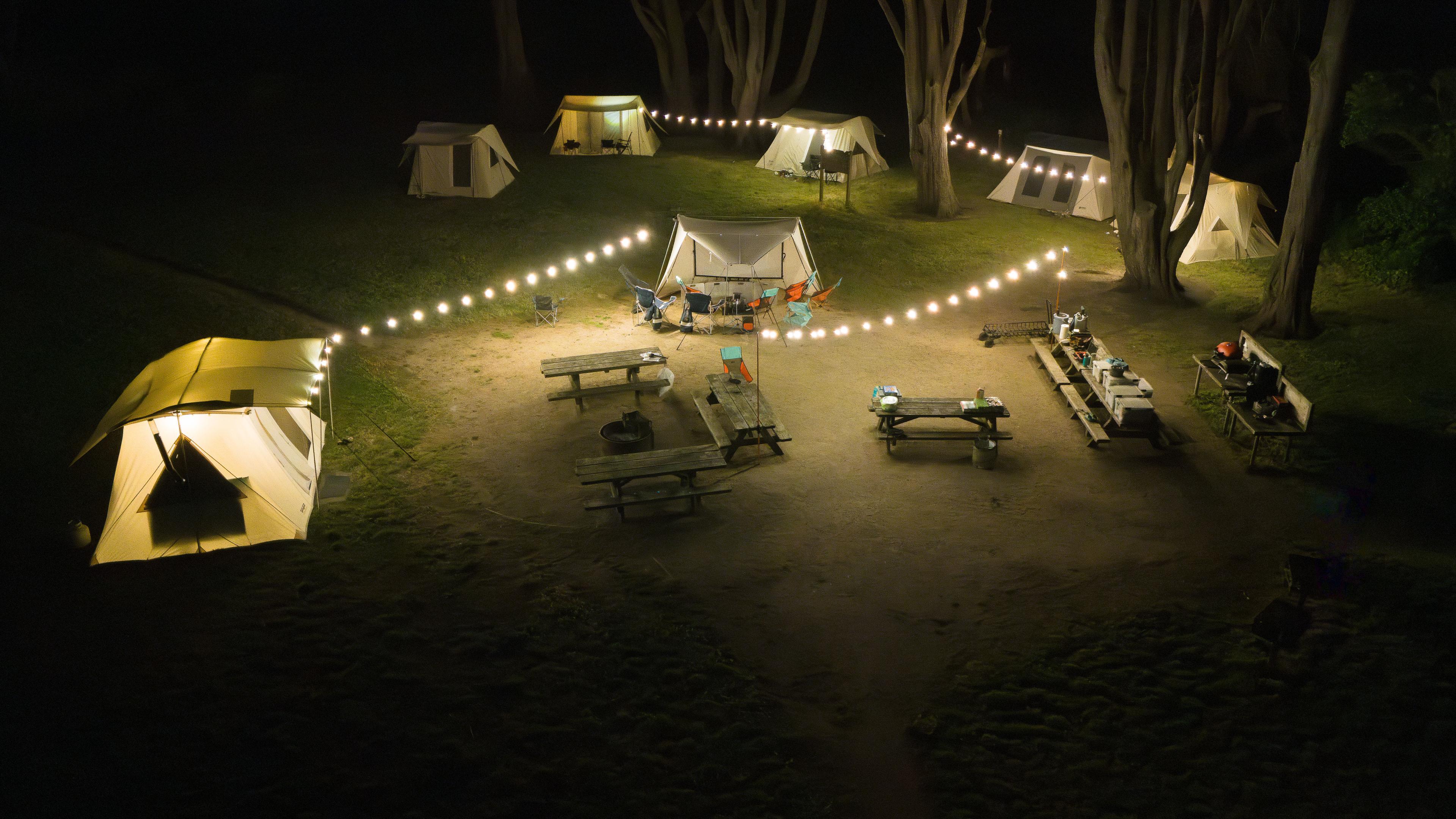 String lights strung across a group campsite at night, canvas tents glowing in the dark String lights strung across a group campsite at night, canvas tents glowing in the dark