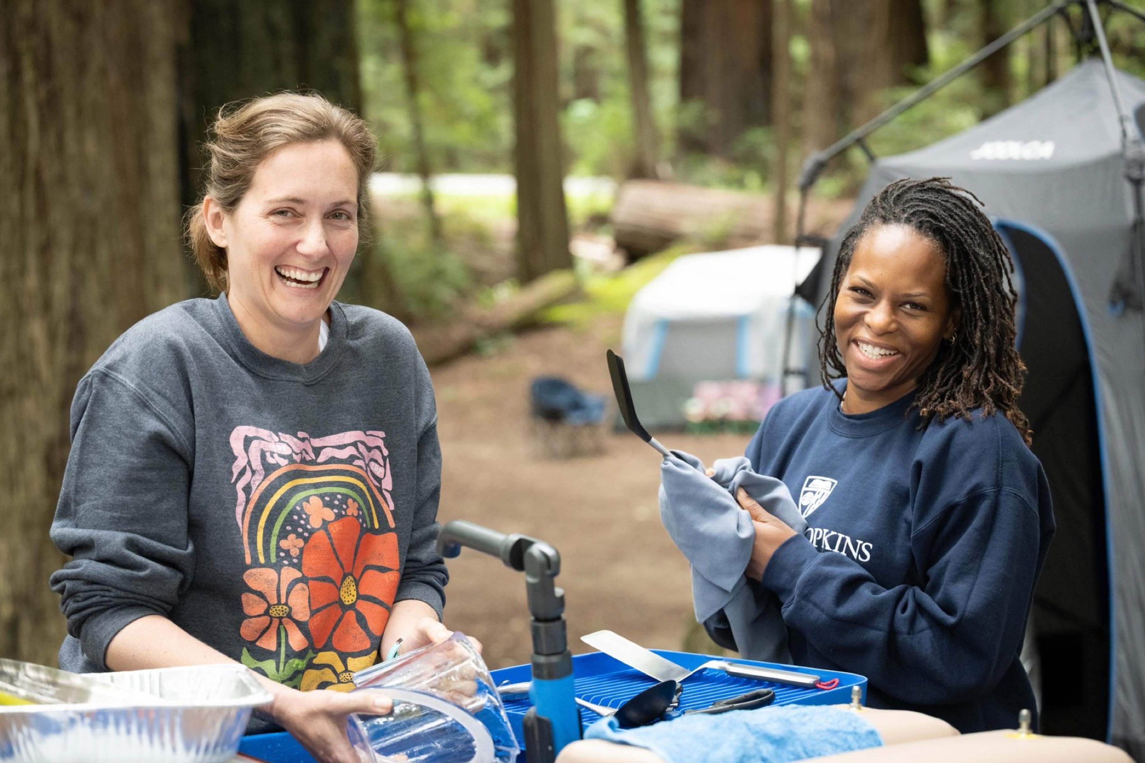 Two campers laughing together while washing dishes at an outdoor wash station at Humboldt Redwoods