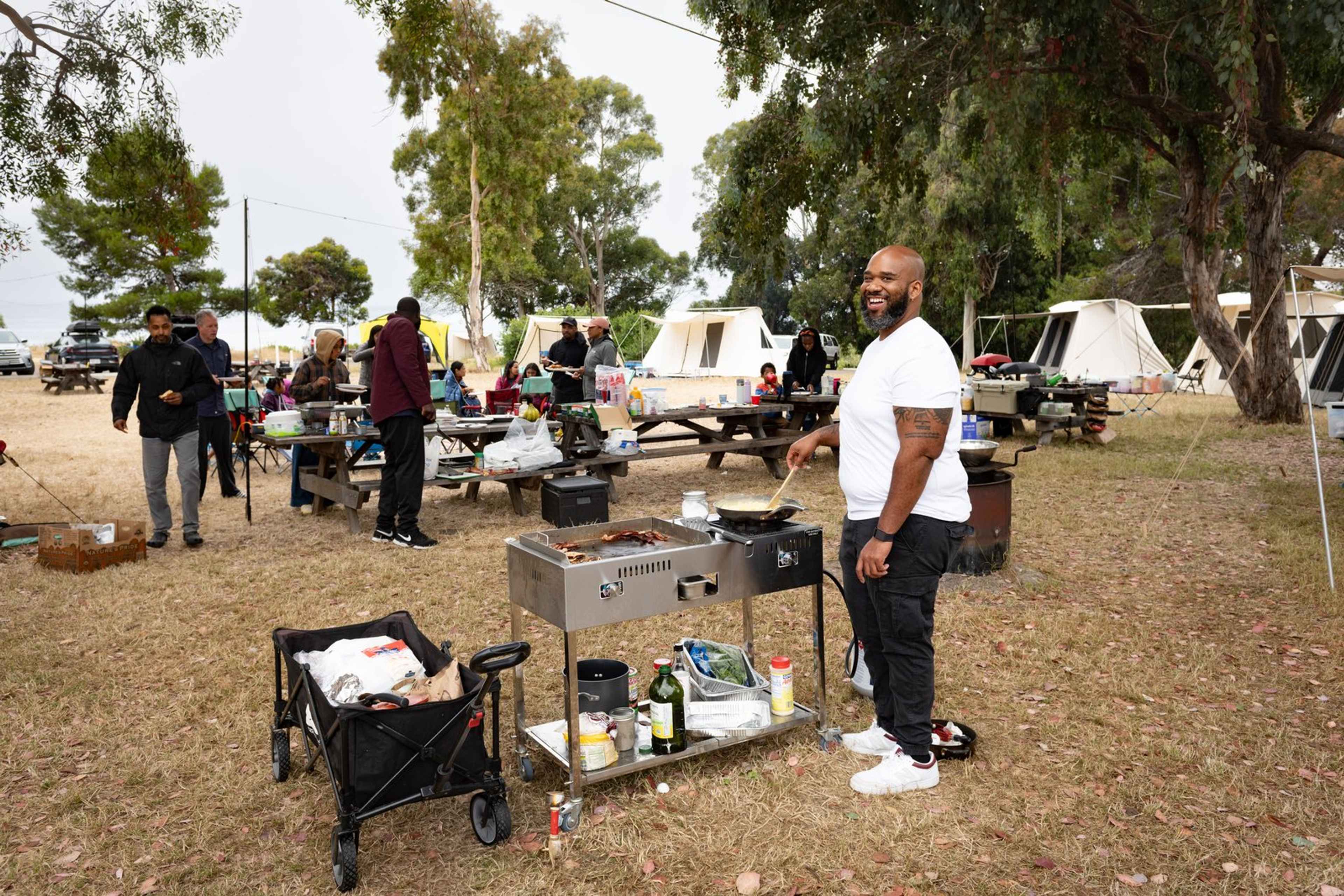 Camper cooking breakfast on a flat-top griddle at an Outdoorithm Collective group campout with canvas tents in the background