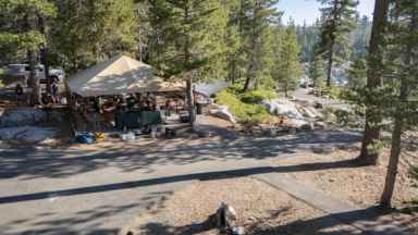 Aerial view of the covered group dining area at Spicer Reservoir group campground, a canvas roof over picnic tables among granite and pines