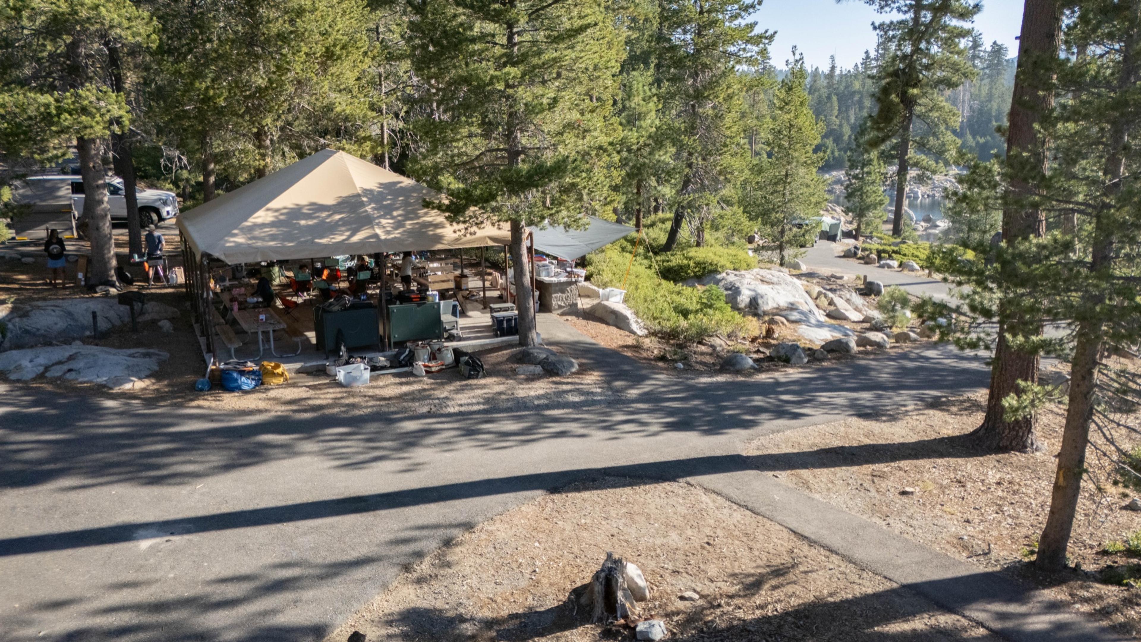 Aerial view of the covered group dining area at Spicer Reservoir group campground, a canvas roof over picnic tables among granite and pines