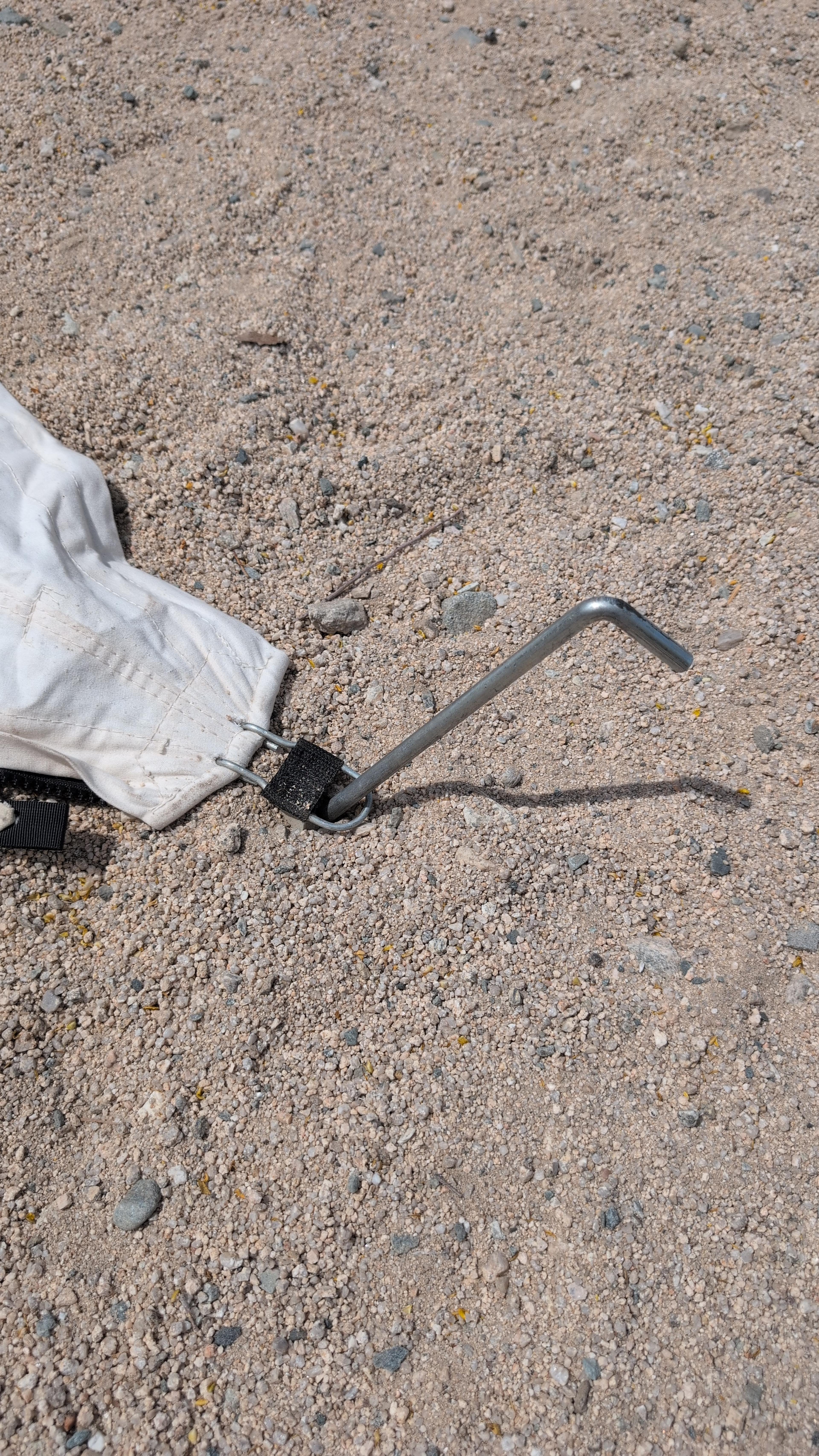 Close-up of a heavy plated-steel L-shaped nail tent stake driven through a ground hook into sandy soil