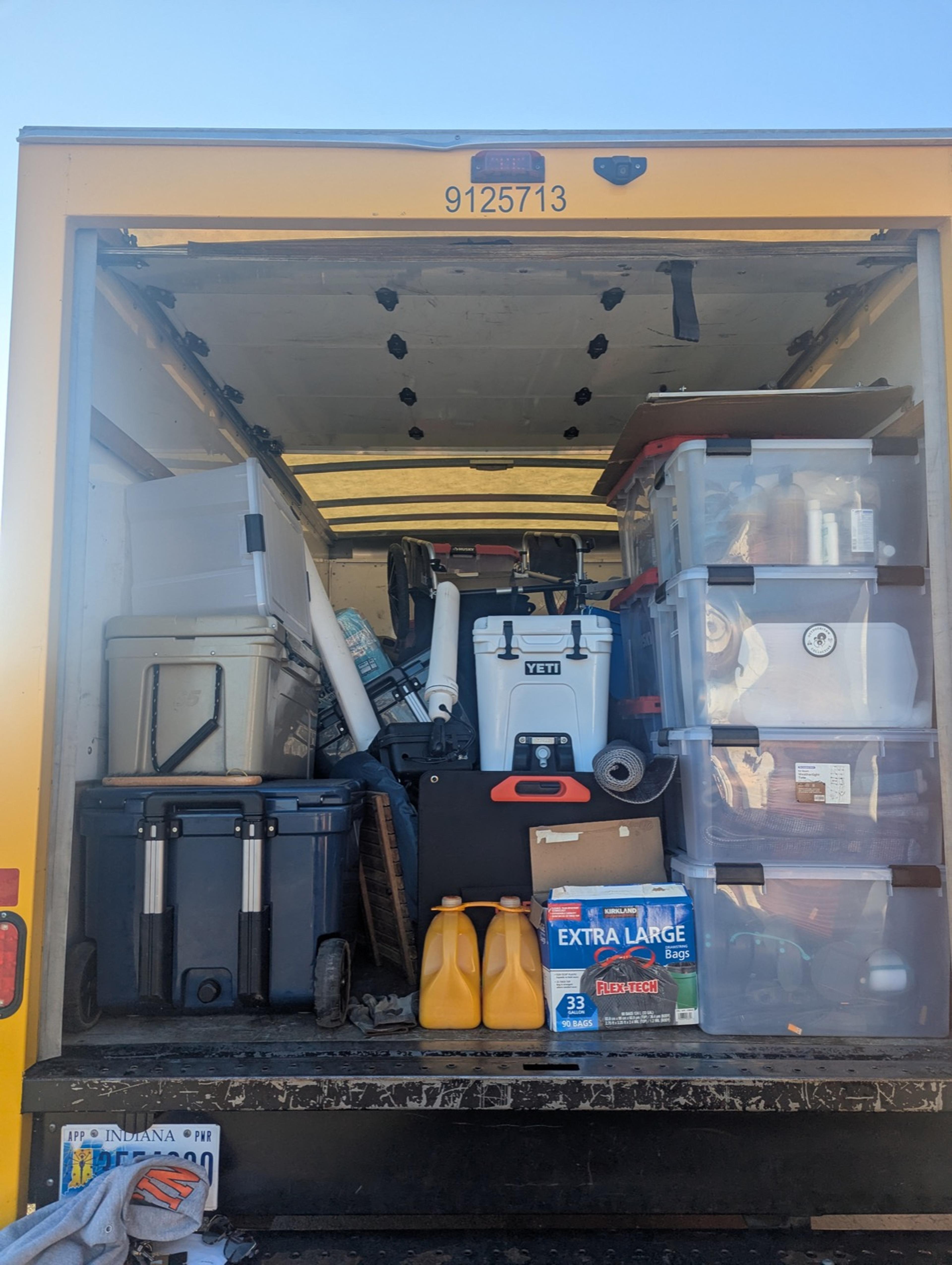 The back of a box truck packed with labeled bins, coolers, and water jugs for a group camping trip The back of a box truck packed with labeled bins, coolers, and water jugs for a group camping trip
