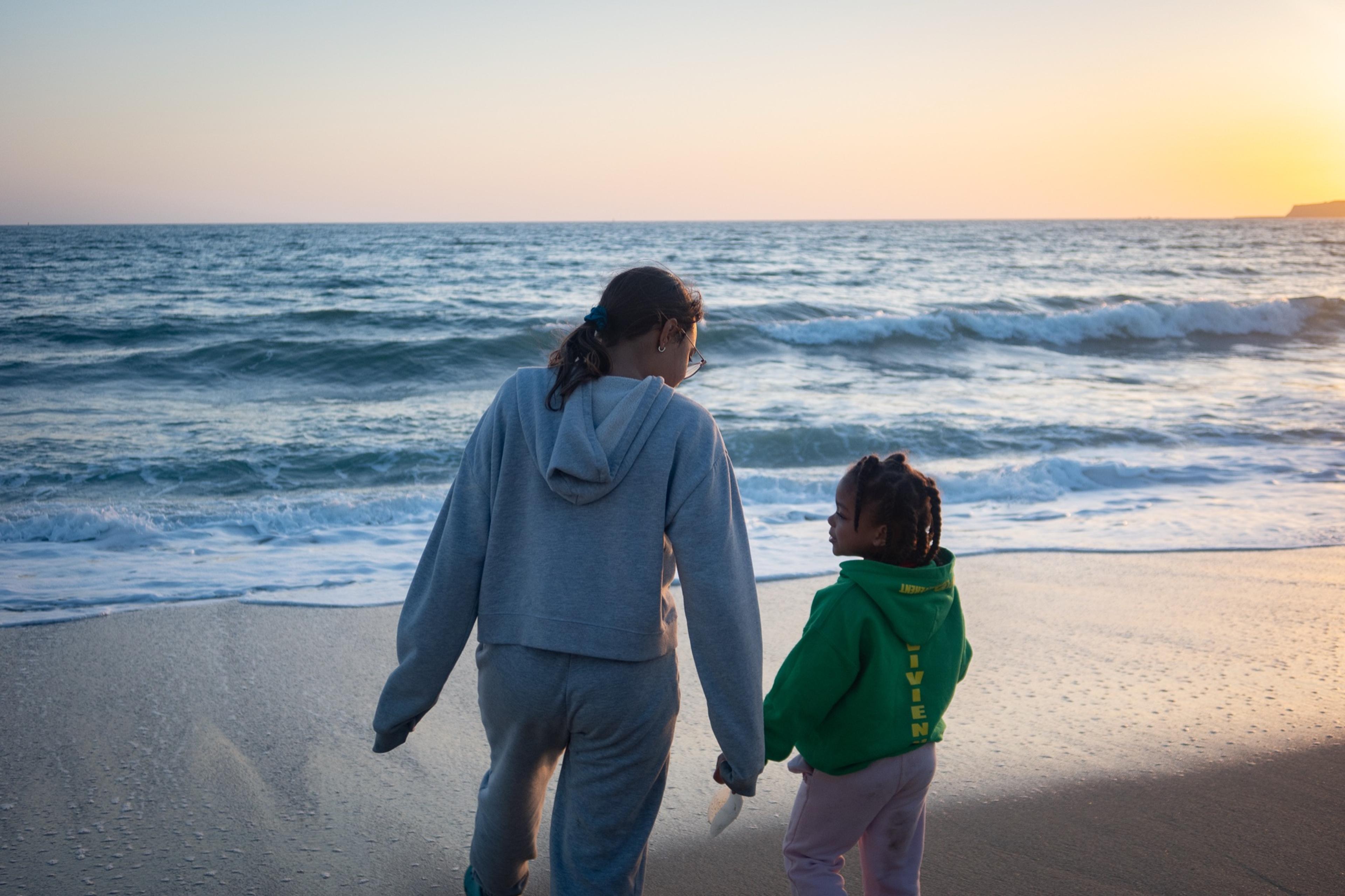 An adult and a small child walking hand in hand along the surf at sunset, seen from behind An adult and a small child walking hand in hand along the surf at sunset, seen from behind