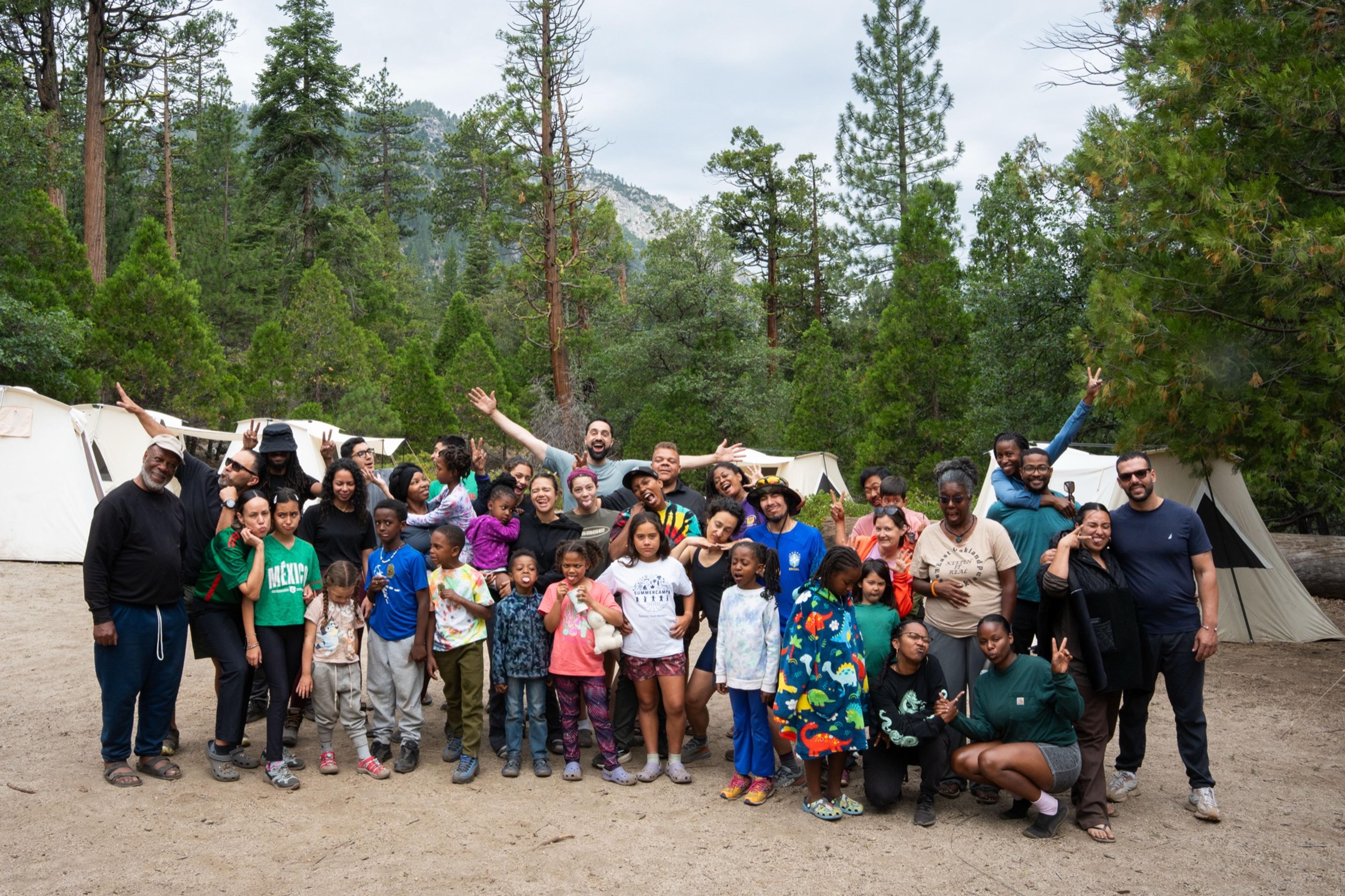 About forty adults and children posed together in front of canvas tents at a Kings Canyon group campsite, arms raised