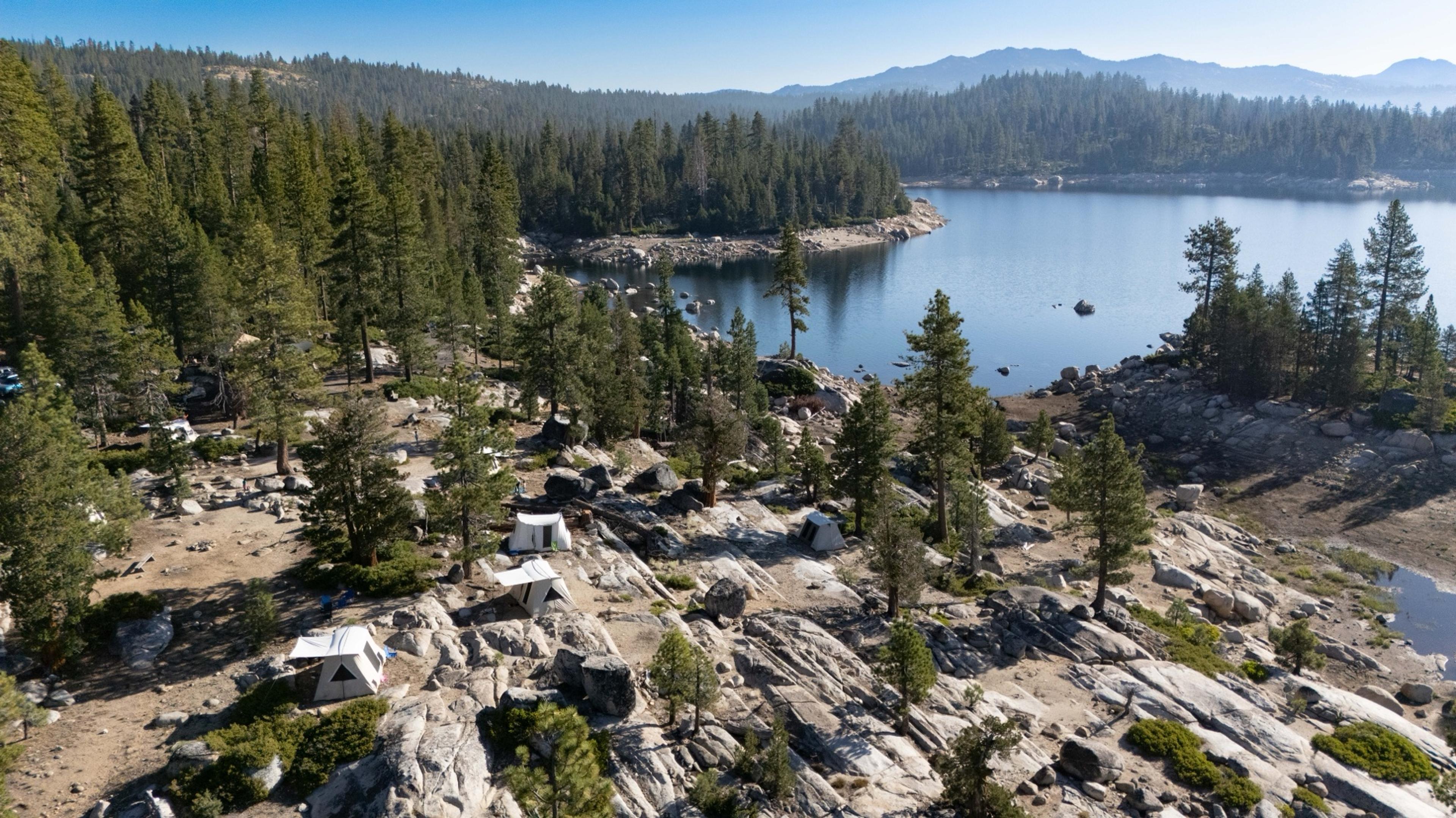 Aerial view of canvas tents pitched among granite slabs at the Spicer Reservoir group campground above a blue Sierra reservoir