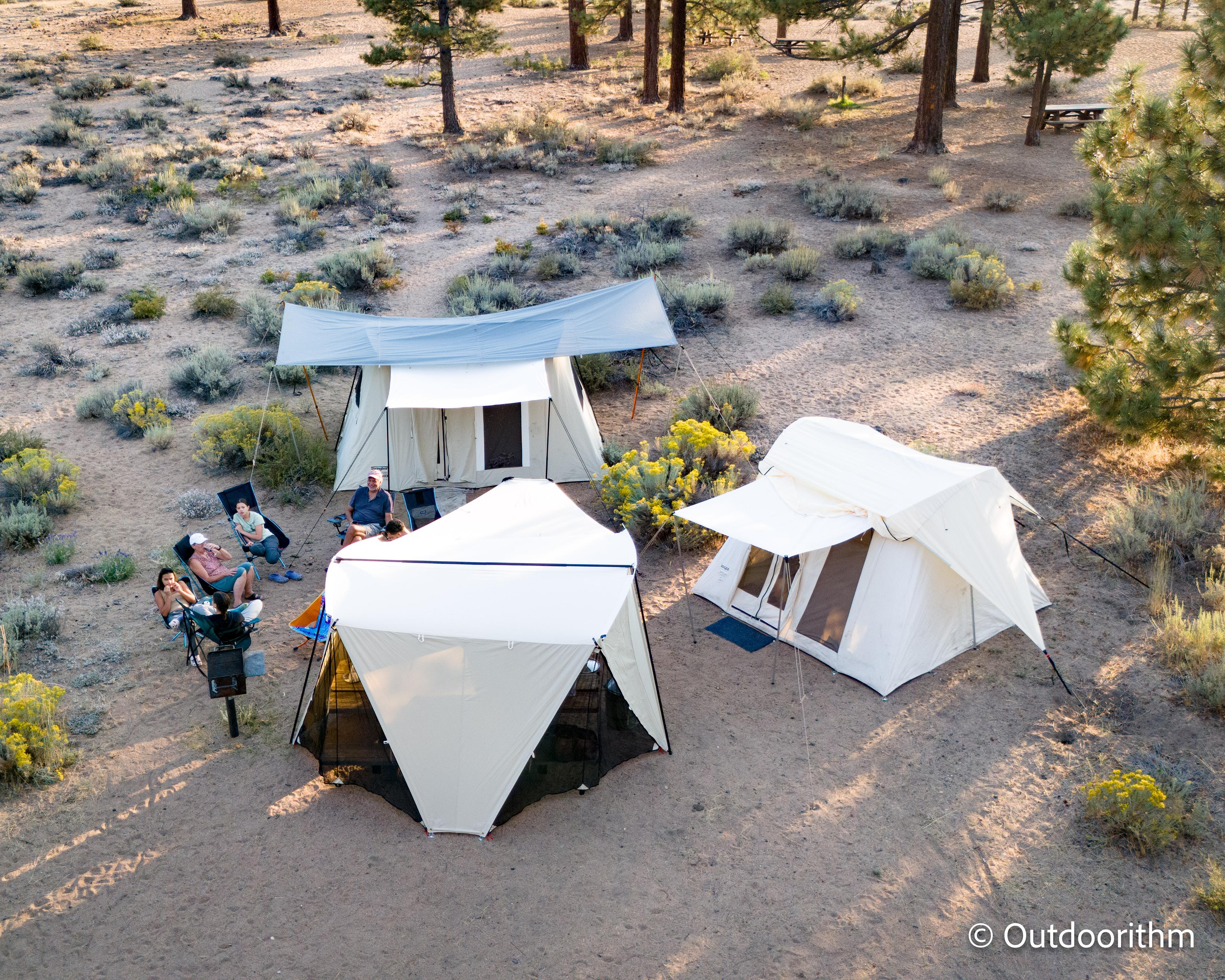 Springbar Classic Jack canvas tent with tarp pitched over it, Springbar Leisure Port shade shelter, and Kodiak Canvas Cabin tent all set up side by side at a Nevada Beach campsite at Lake Tahoe surrounded by pine trees, with Justin seated in a camp chair in the foreground