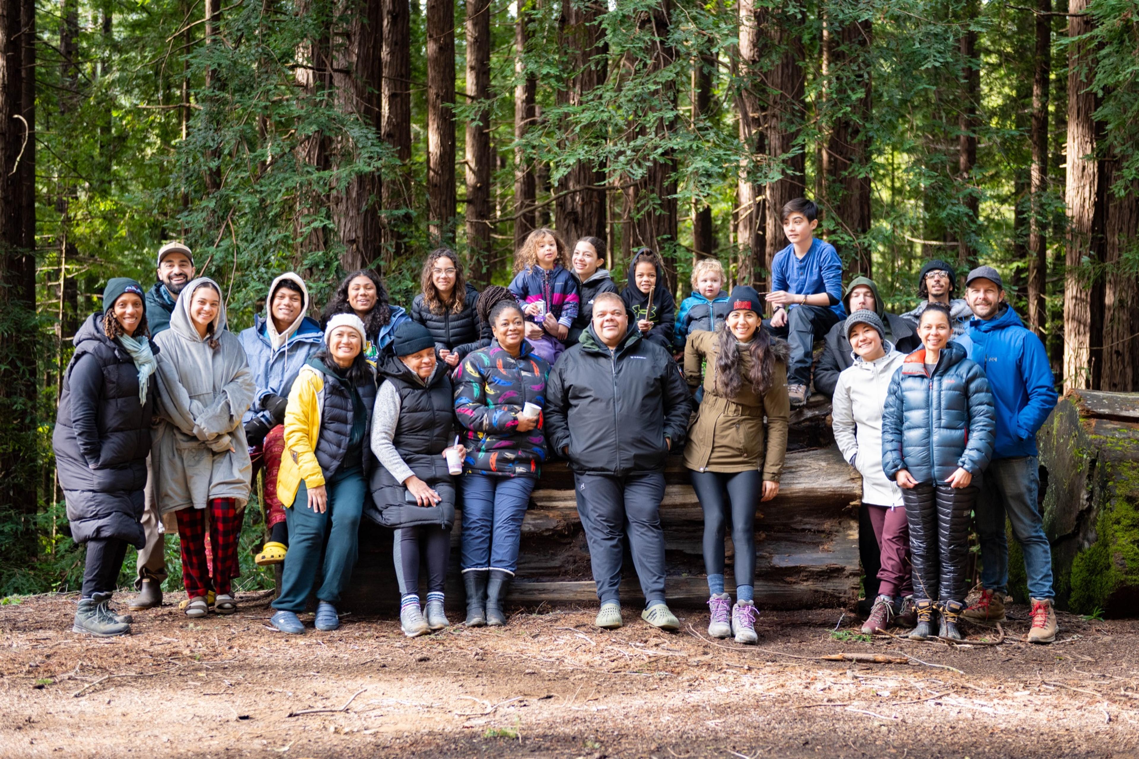 A group of adults and kids in down jackets and beanies posed on a fallen redwood log in the forest A group of adults and kids in down jackets and beanies posed on a fallen redwood log in the forest