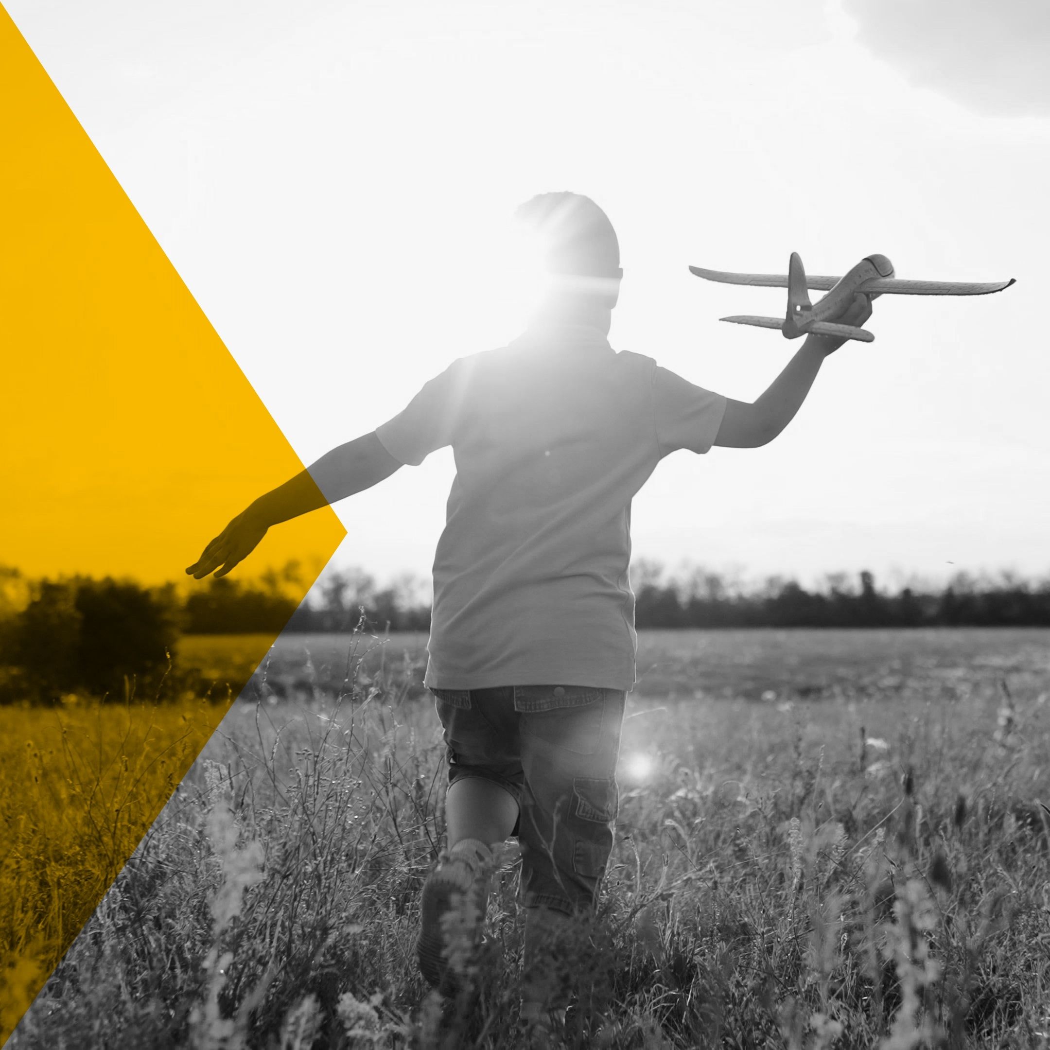 Young boy running through a field with a model airplane in his right hand.