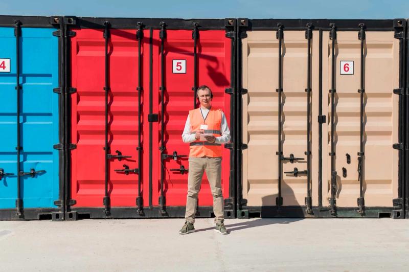 Person i oransje refleksvest med nettbrett foran en rød lagercontainer på et minilager-anlegg.