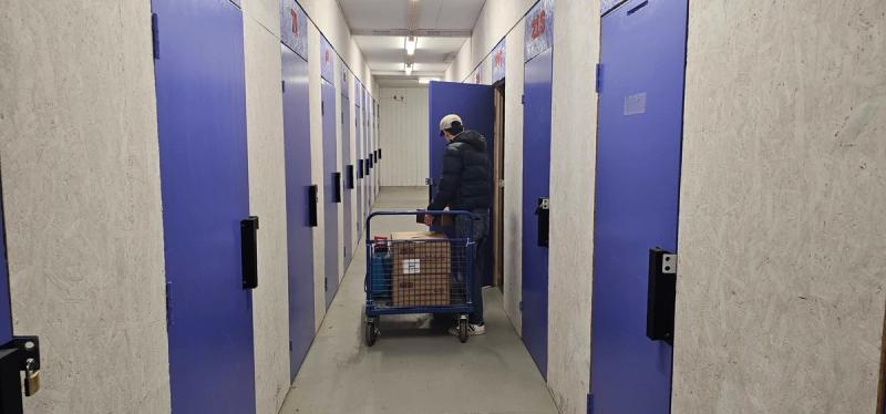 Person triller en tralle med pappesker i en innendørs korridor med blå lagerboder