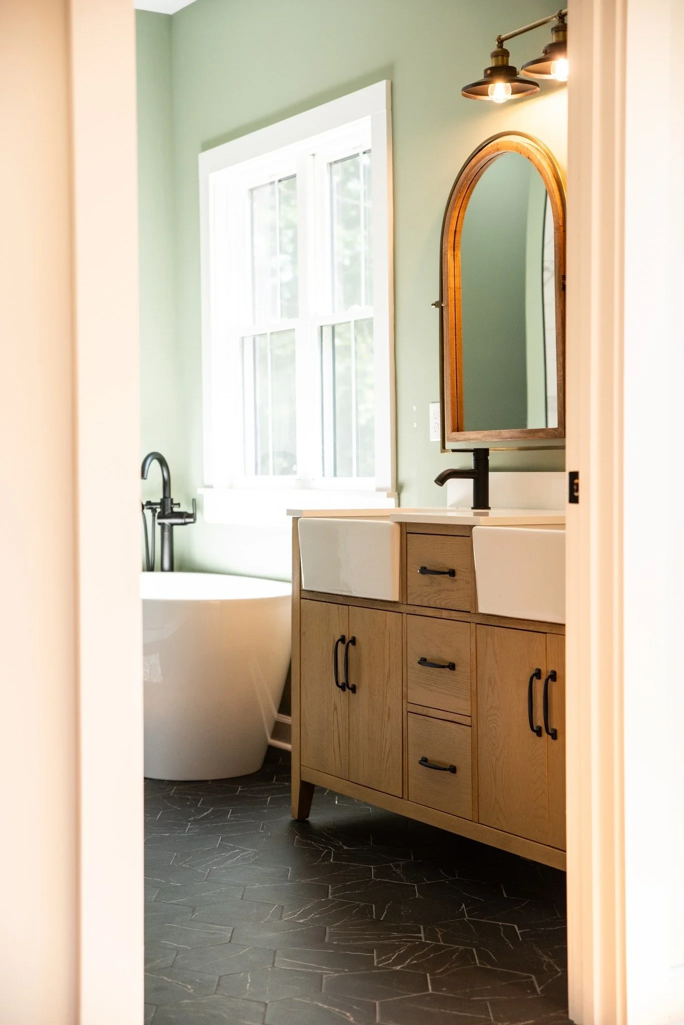 Bathroom with green walls, a large window, freestanding tub, and wood vanity