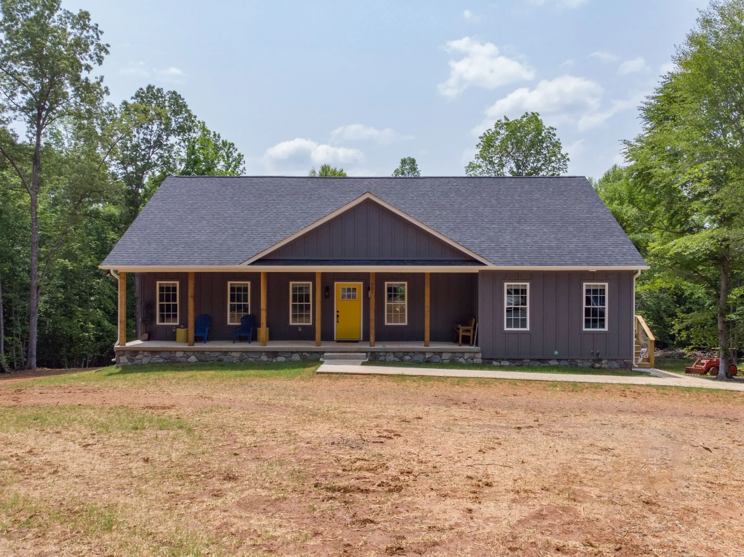 A newly built house with a gray exterior, a yellow front door, and a front porch, set among trees.