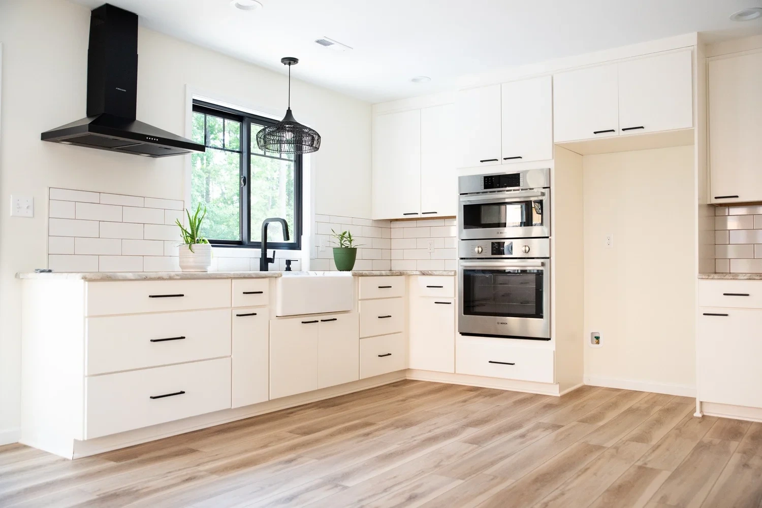 Remodeled kitchen with white cabinets, a black range hood, and a double oven