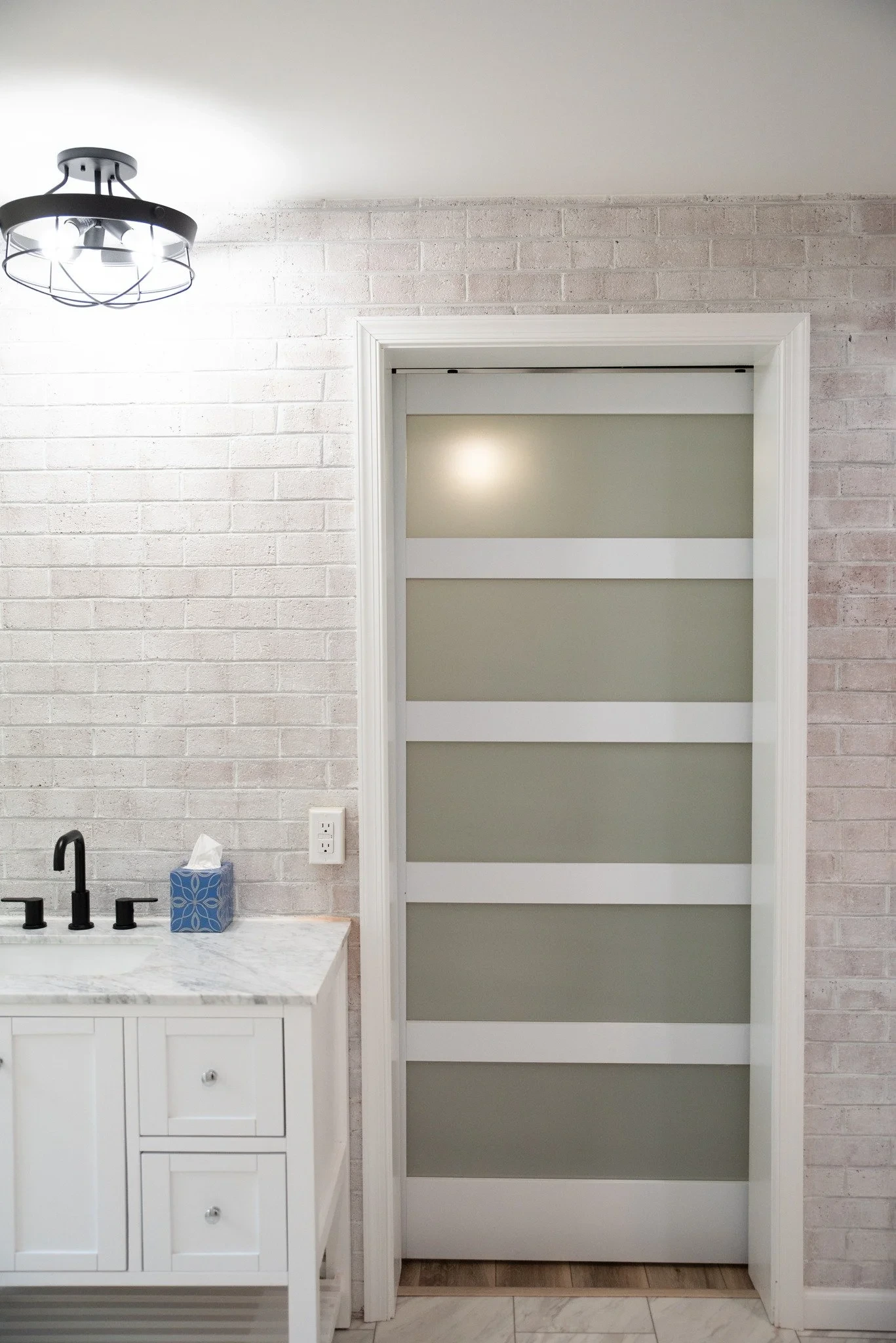Bathroom with a white brick wall, marble countertop, and black fixtures