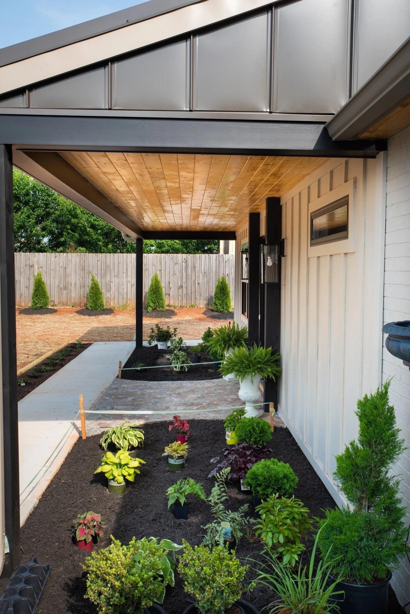 House porch with a wooden ceiling, potted plants, and young shrubs