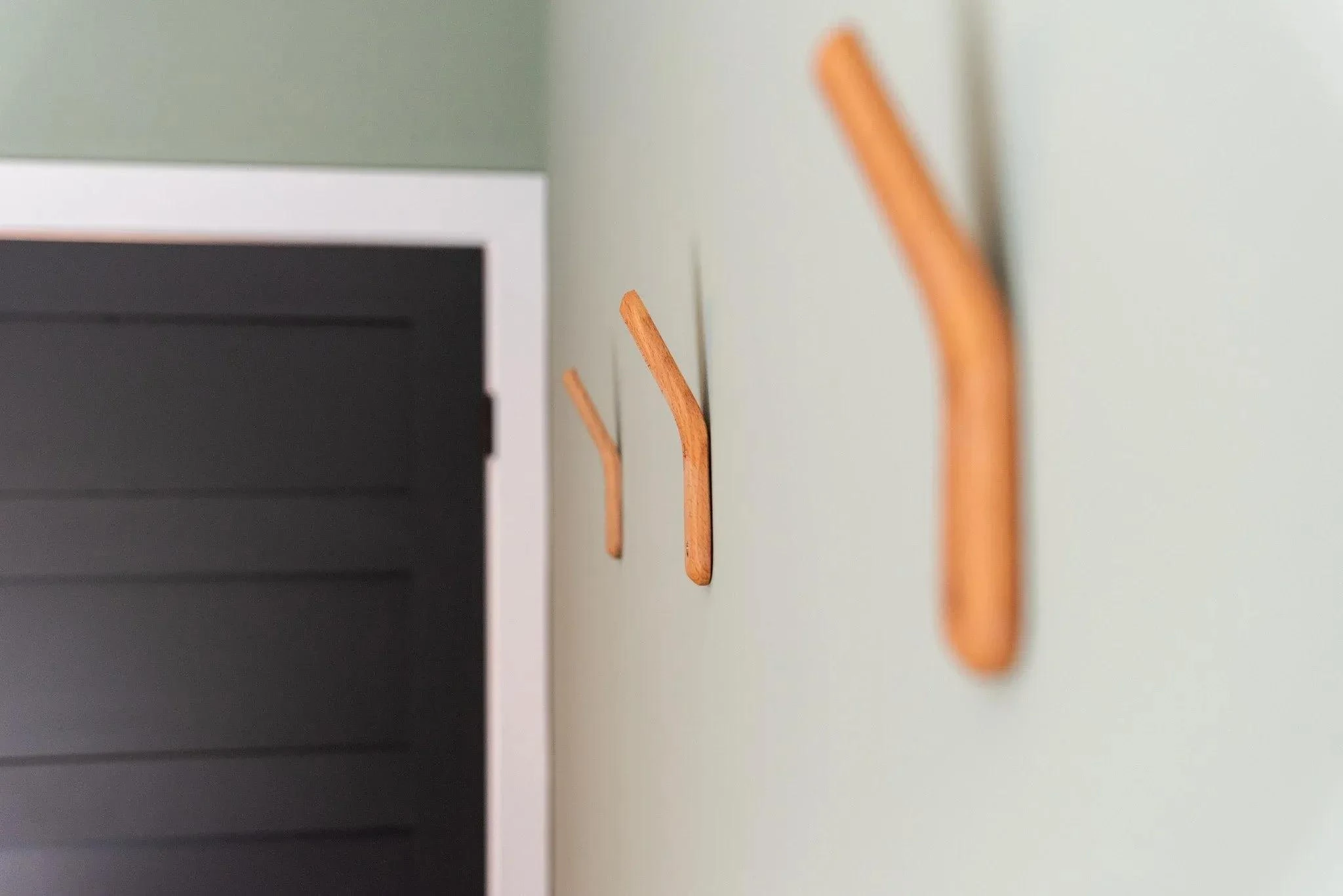 Close-up of three wooden hooks mounted on a green wall, with a partial view of a white and black object on the left.