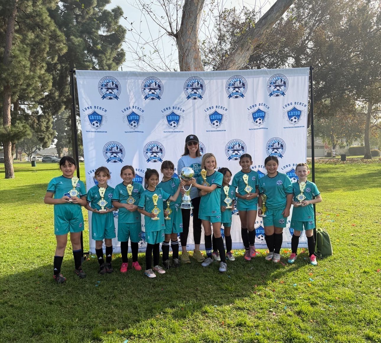 The Girls U10 team in teal uniforms holding their championship trophies in front of an LBYSO banner.