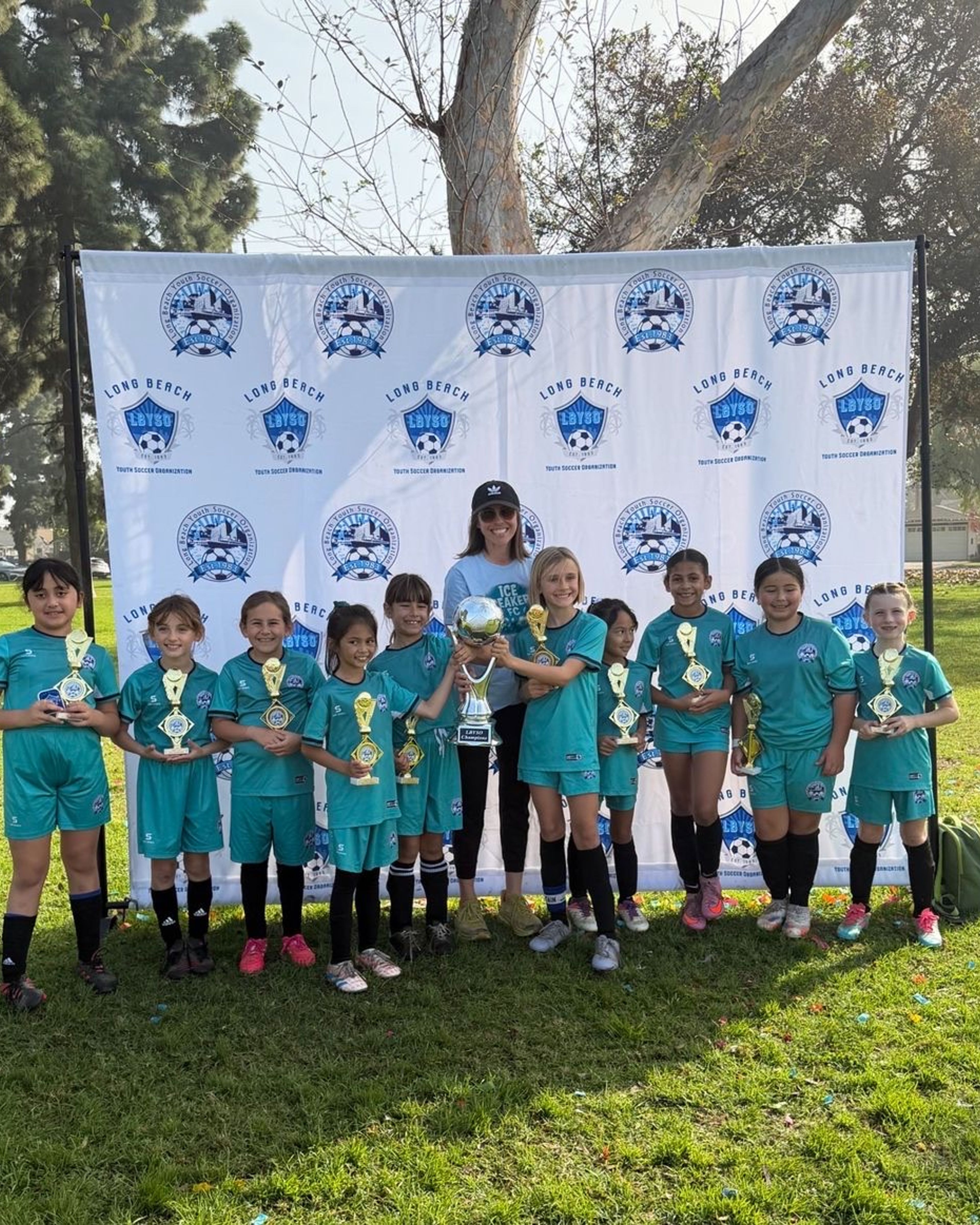 The Girls U10 team in teal uniforms holding their championship trophies in front of an LBYSO banner.
