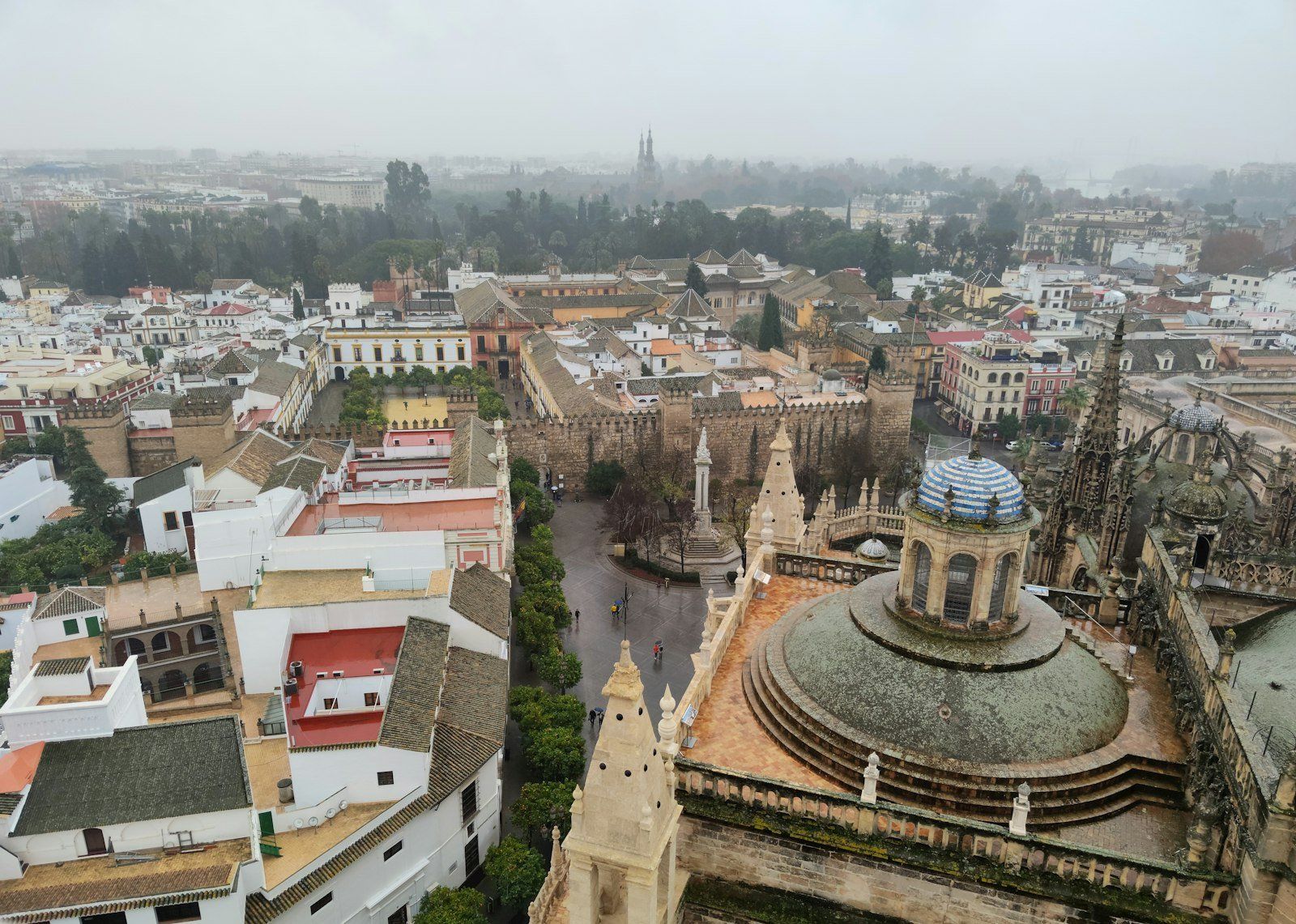 Vista panorámica de Sevilla con la Catedral y la Giralda, murallas almohades, plaza con monumento y edificios históricos nublados