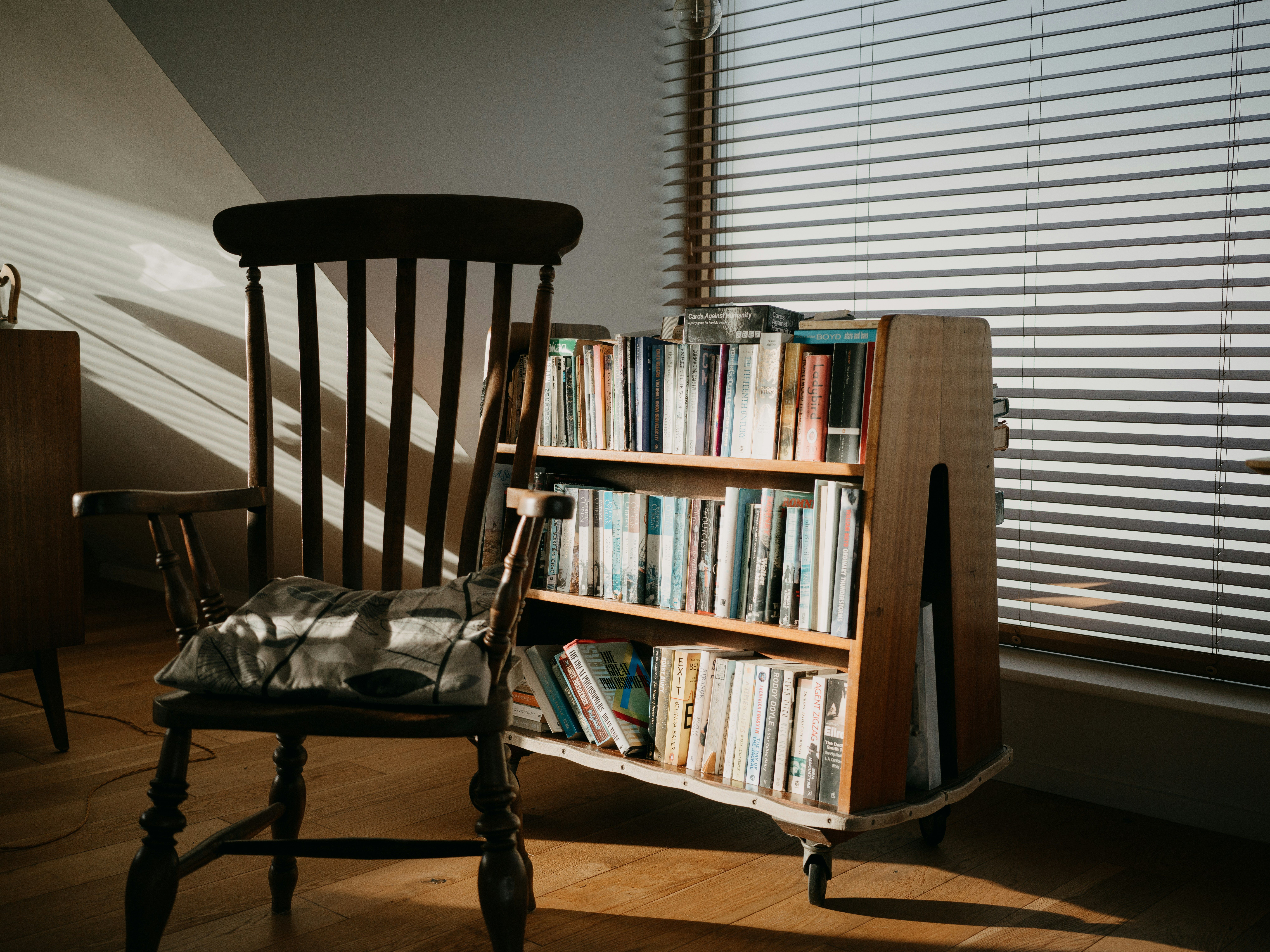 Una silla de madera y una estantería con libros junto a una ventana con persianas.