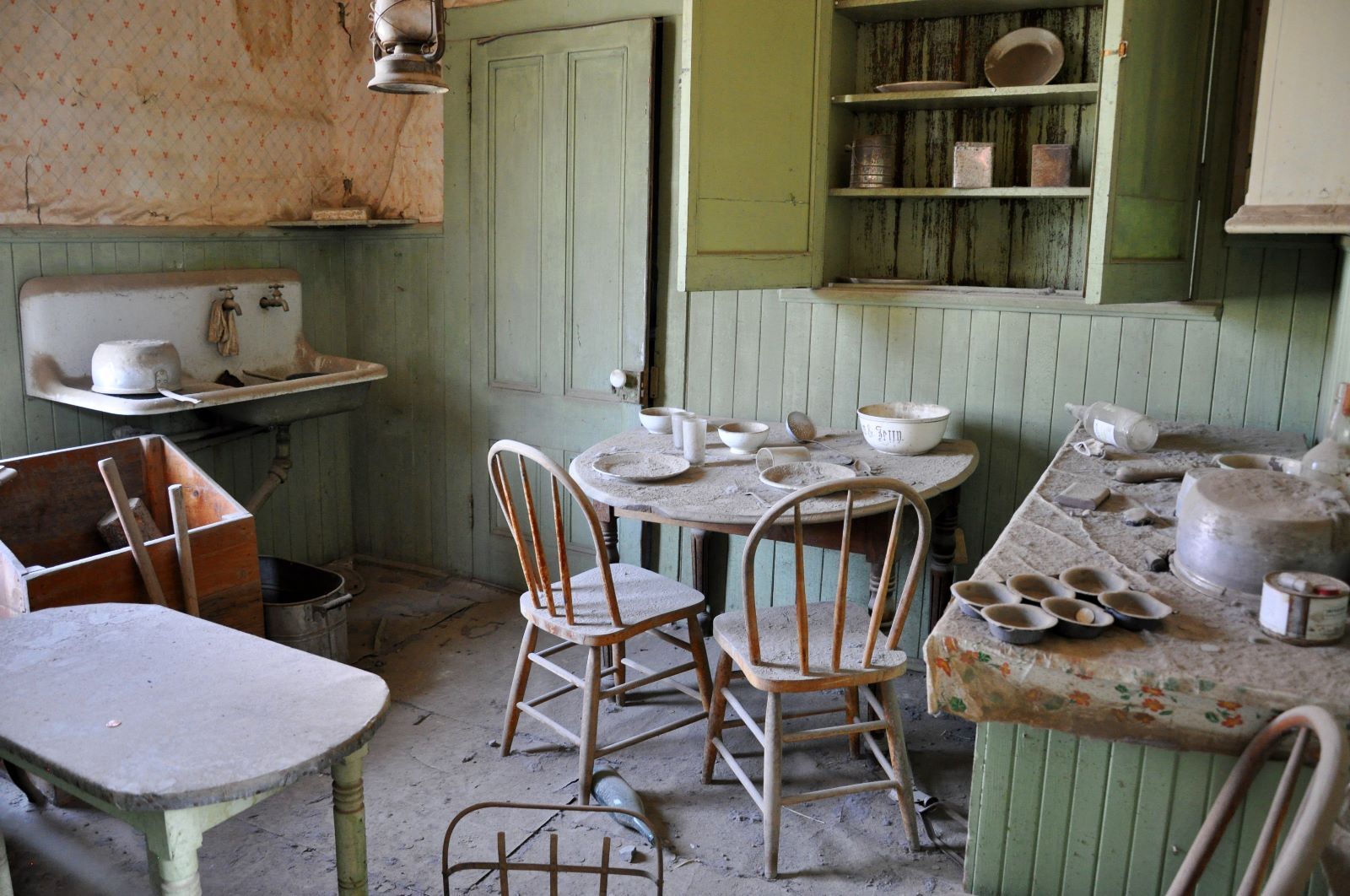 Interior de una cocina polvorienta y abandonada con muebles de madera, fregadero y utensilios.