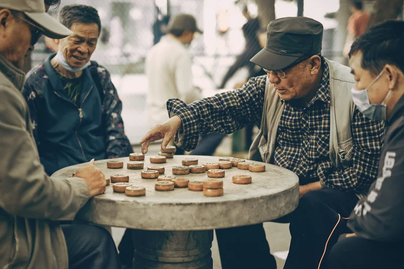Cuatro hombres chinos jugando al ajedrez chino en una mesa redonda de piedra al aire libre.