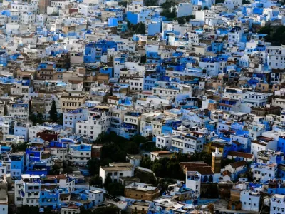 Vista aérea de la medina de Chefchaouen, con casas azules y blancas apiladas en la colina, tejados rojos y vegetación esparcida