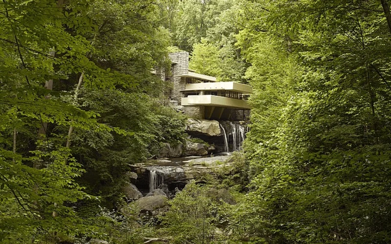 La casa Fallingwater se integra en un bosque frondoso, con terrazas cantileveradas sobre una cascada rocosa