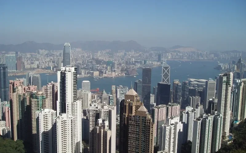 Vista panorámica del skyline de Hong Kong desde Victoria Peak, con rascacielos altos, puerto Victoria y montañas al fondo bajo cielo azul