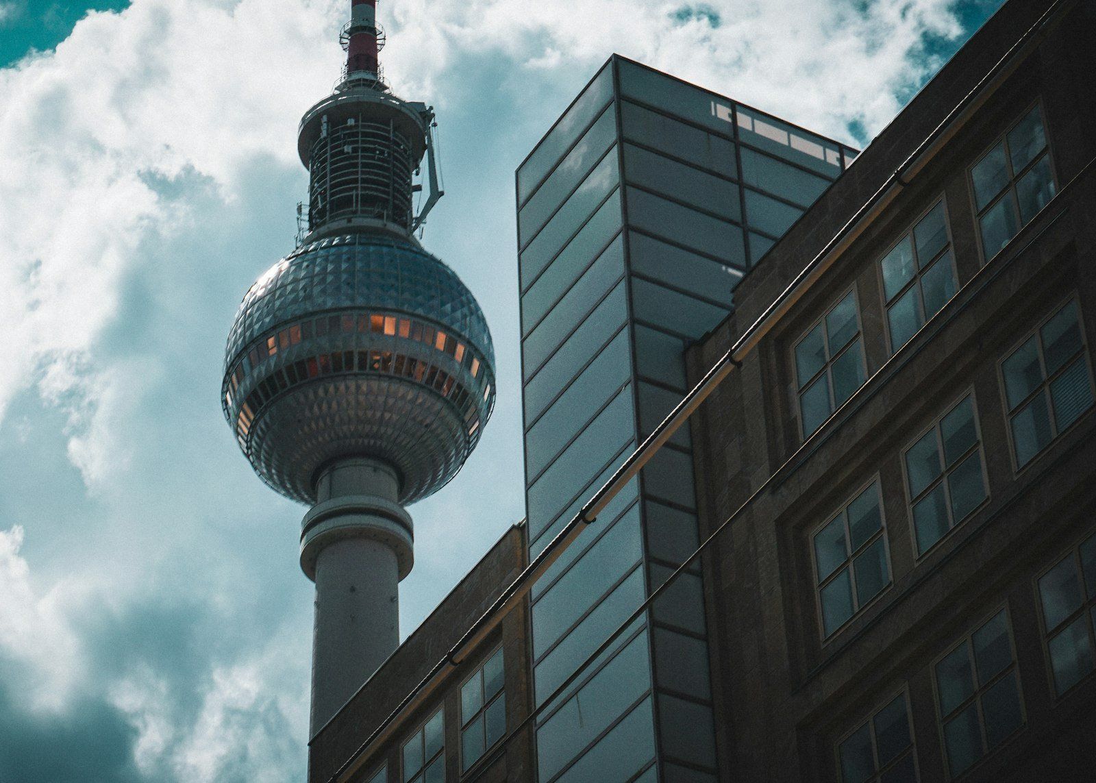 La Torre de Televisión de Berlín destaca con su esfera plateada sobre edificios modernos de vidrio y ladrillo, bajo un cielo parcialmente nublado con