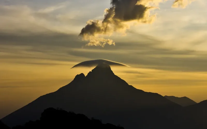 Silueta de un volcán con nubes en forma de sombrero sobre su cima al atardecer en el Parque Nacional de Virunga