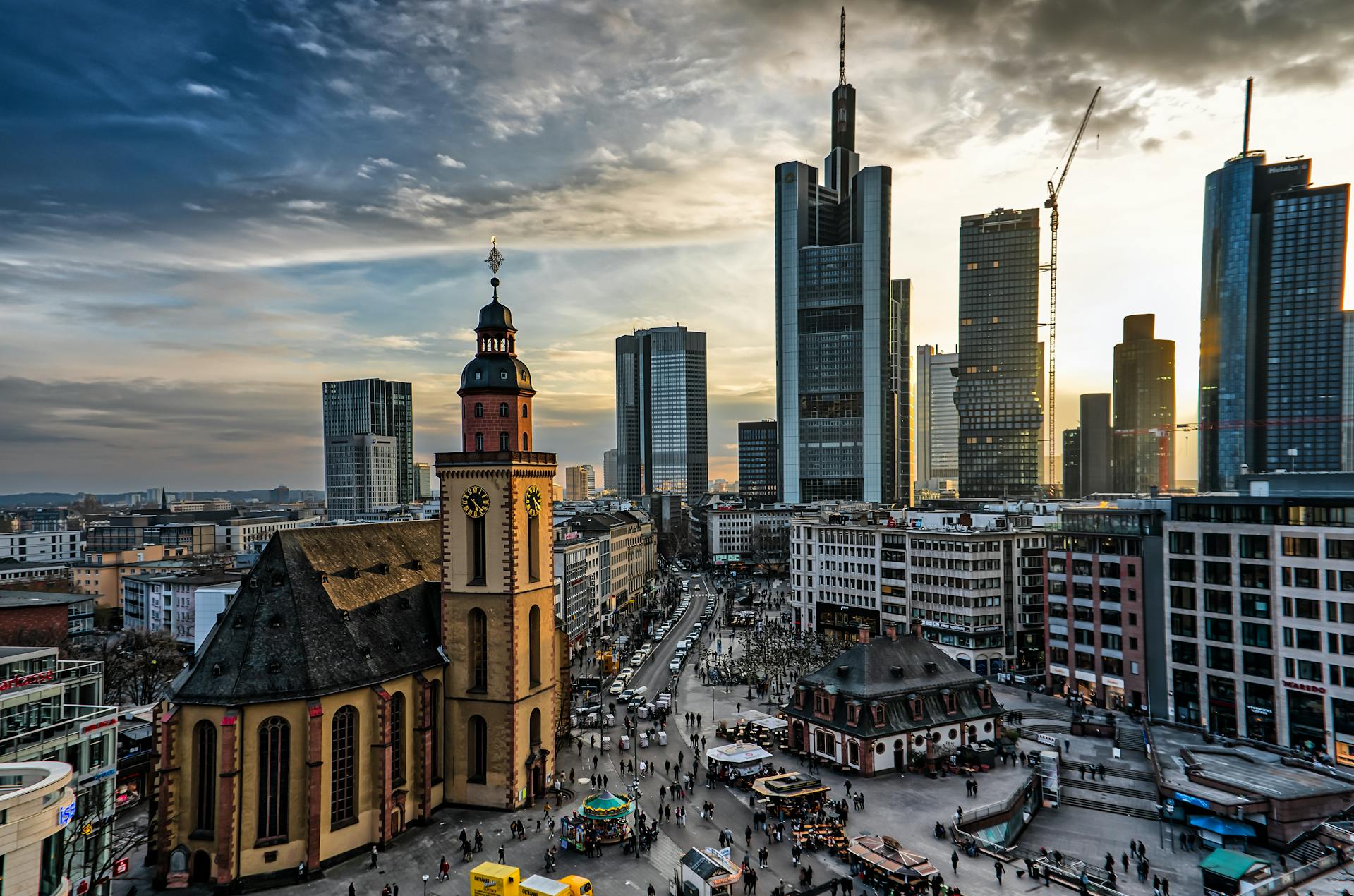 Panorama de Römerberg en Frankfurt con iglesia roja histórica, plaza animada con gente y puestos, y rascacielos modernos al atardecer