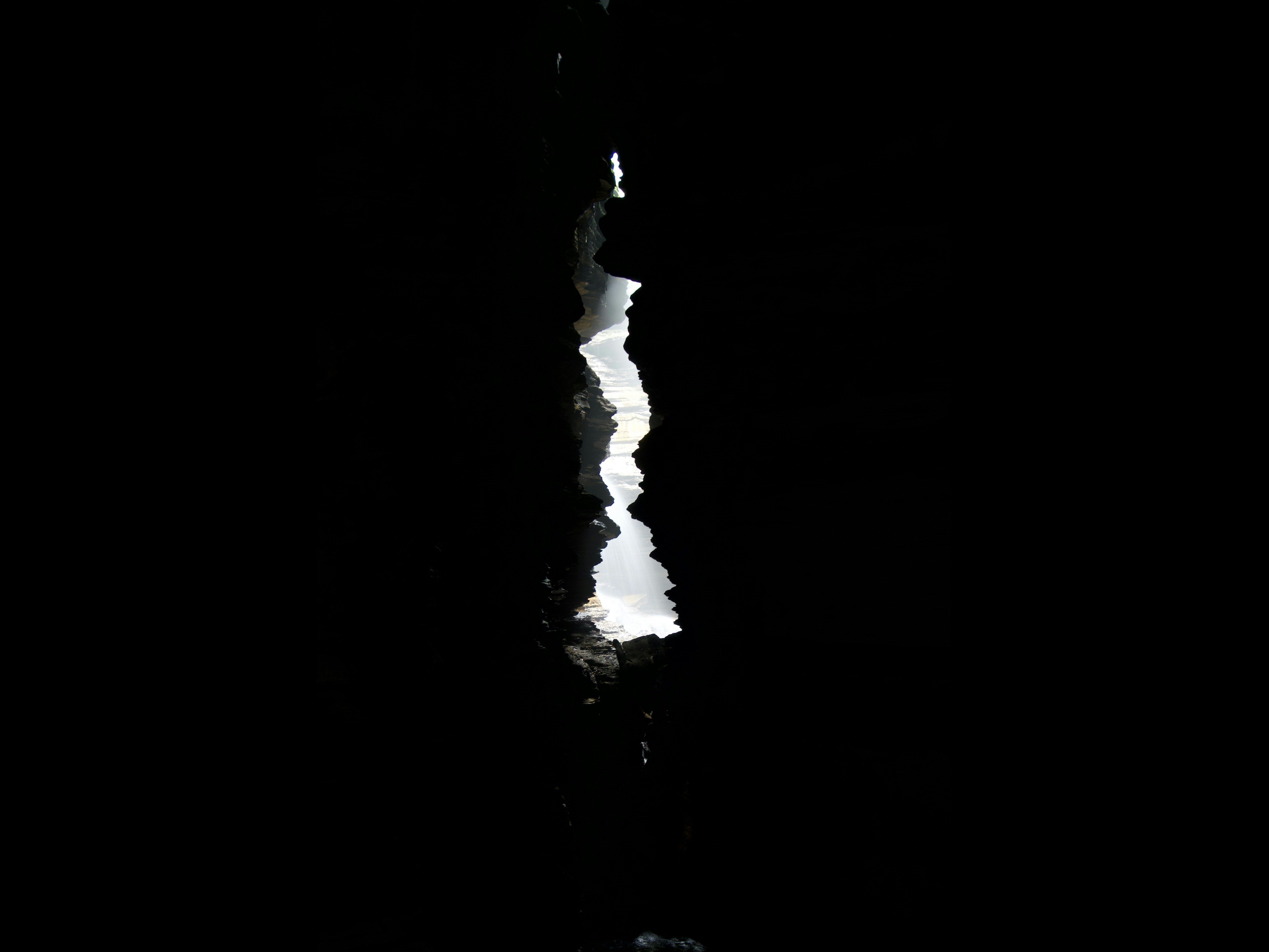 Una grieta vertical estrecha y luminosa en una superficie oscura, revelando luz brillante al fondo.