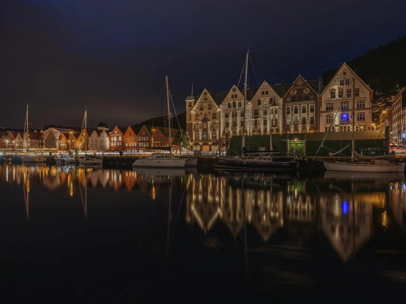 Vista panorámica de Bryggen, el histórico muelle hanseático de Bergen con sus características casas de madera coloridas reflejándose en el puerto de Vågen, rodeado de montañas verdes