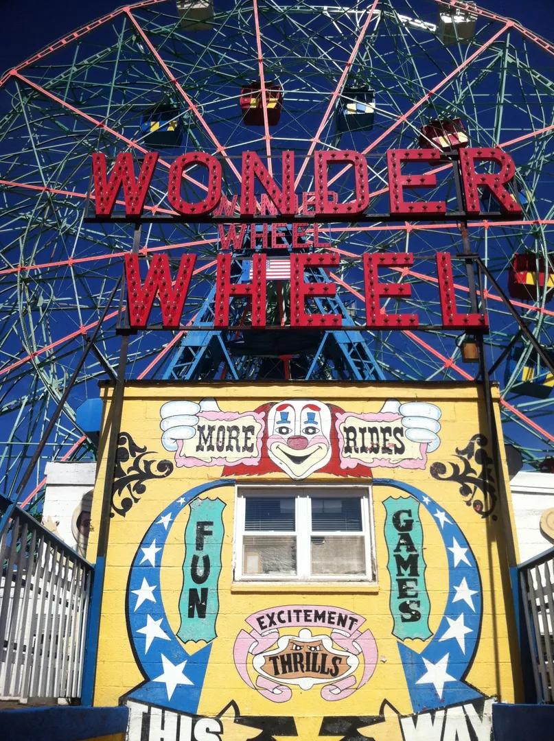 Rueda de la fortuna Wonder Wheel iluminada en rojo sobre un edificio amarillo con letreros de diversión y emociones en Coney Island