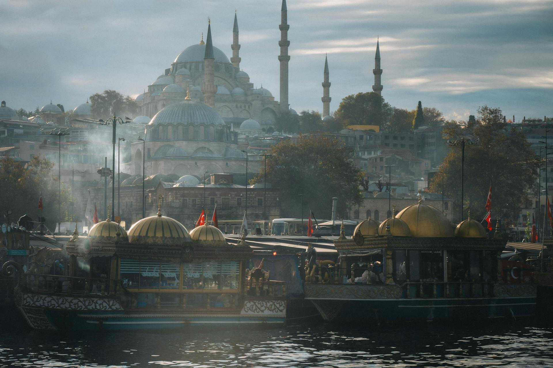 Vista de Estambul con la Mezquita Azul y minaretes en el fondo nublado, y barcos con techos dorados y banderas turcas en primer plano
