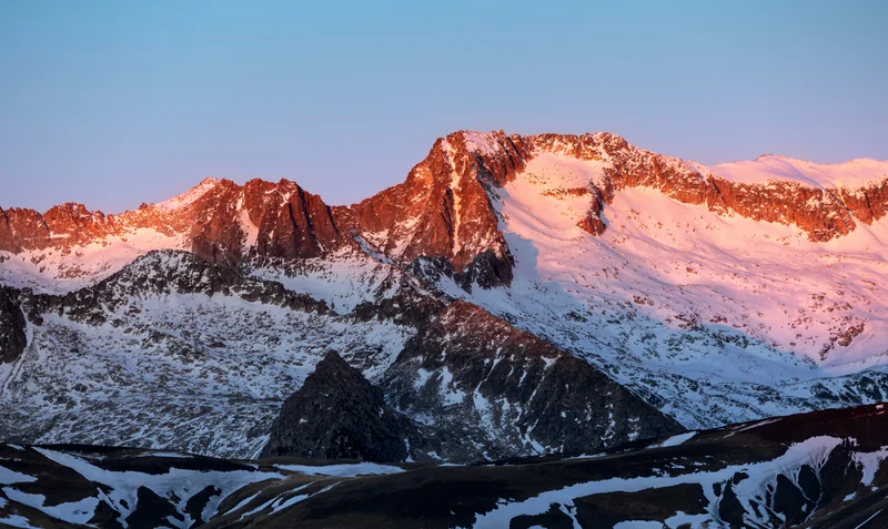 Cumbres montañosas nevadas iluminadas por el sol del amanecer o atardecer.