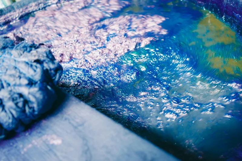 Tela teñida de azul oscuro junto a un baño de tinte índigo burbujeante.