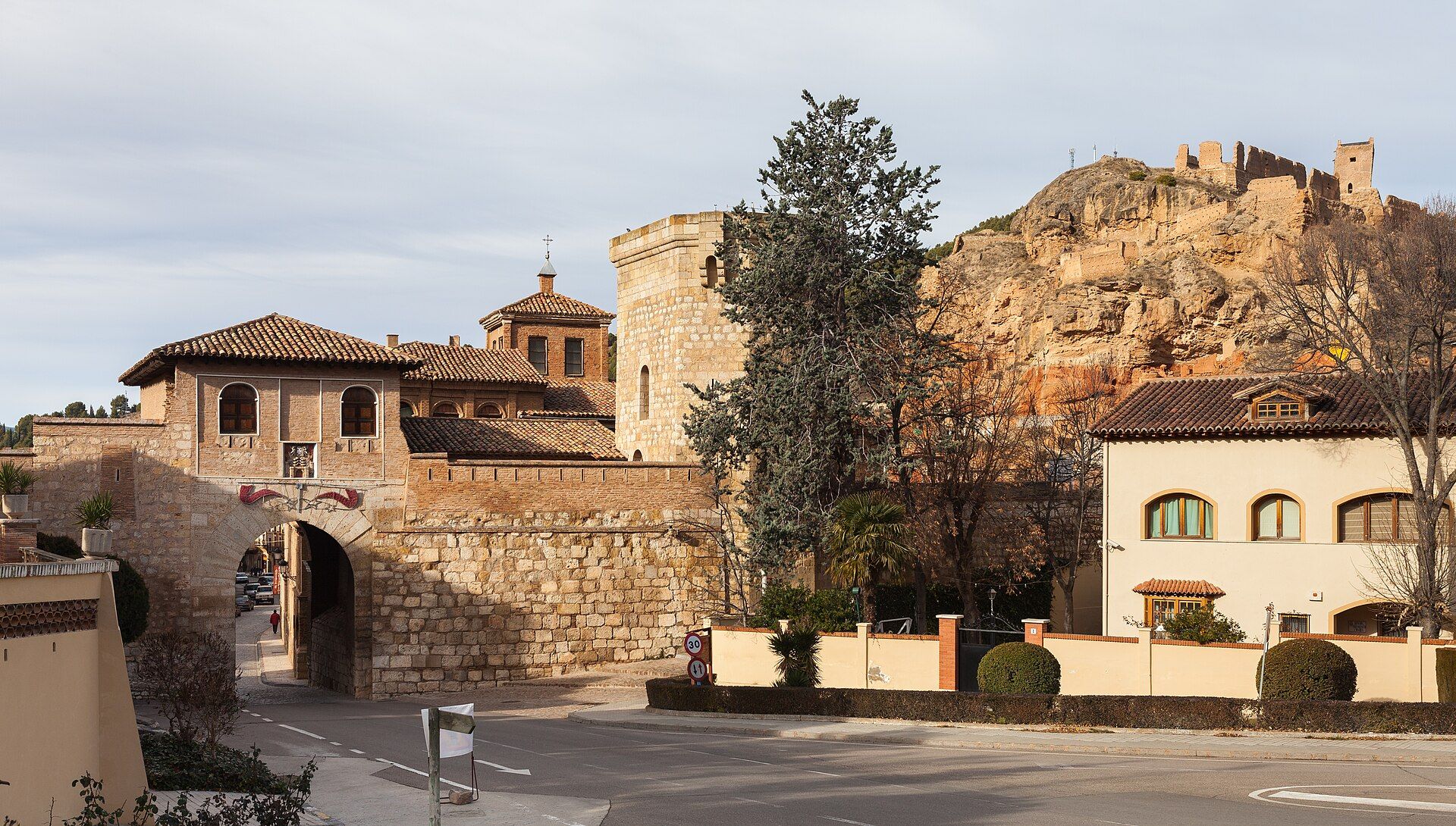 Vista exterior de la Puerta Alta de Daroca con un castillo en la cima de una colina rocosa.