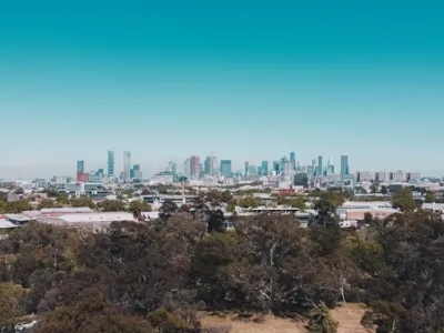 Vista panorámica de Melbourne con skyline de rascacielos altos bajo un cielo azul claro, con árboles y vegetación en primer plano