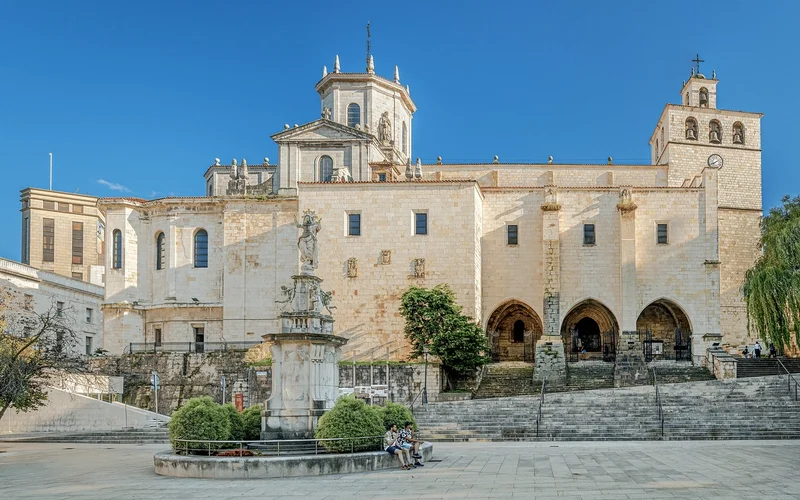 La catedral de Santander con su fachada de piedra clara, torres y arcos góticos, frente a una fuente ornamentada en la plaza bajo cielo azul