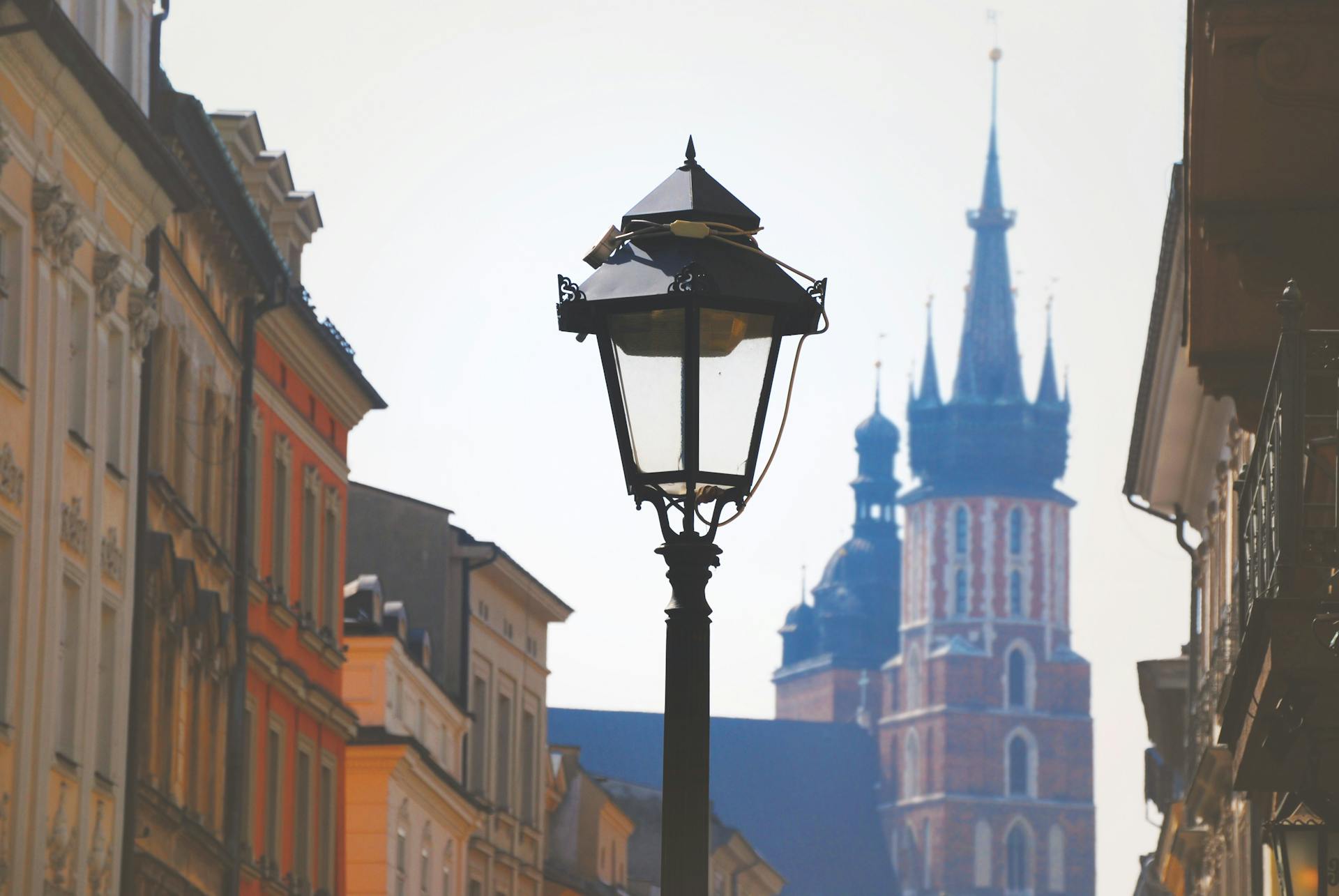 Farola antigua en calle histórica de Cracovia, con edificios coloridos y la basílica de Santa María al fondo