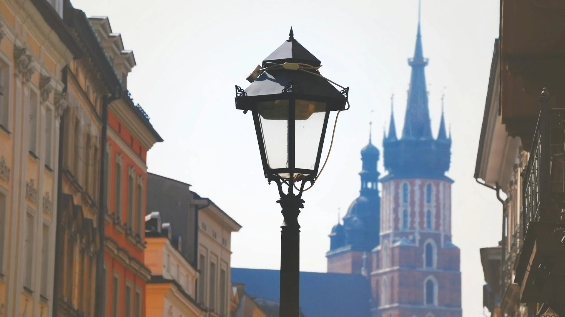 Vista de una calle antigua en Cracovia con farola de hierro y la torre gótica de la Basílica de Santa María al fondo