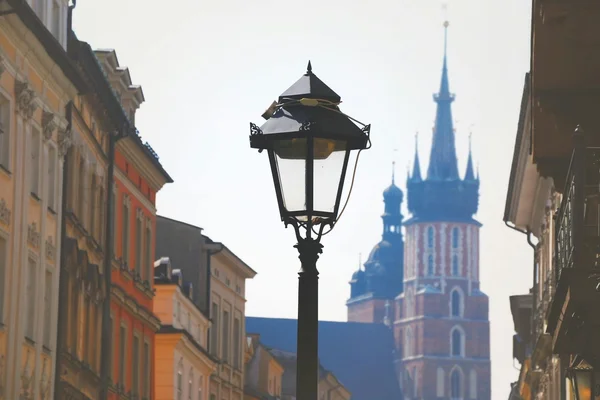 Vista de una calle antigua en Cracovia con farola de hierro y la torre gótica de la Basílica de Santa María al fondo