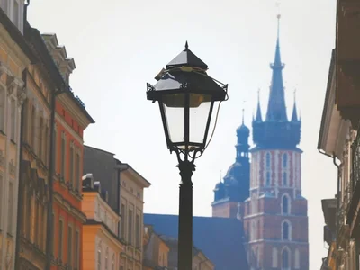 Farola antigua en calle histórica de Cracovia, con edificios coloridos y la basílica de Santa María al fondo
